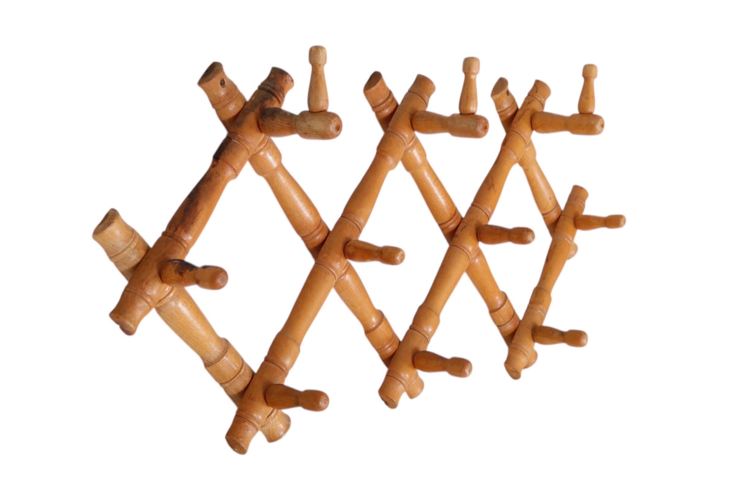 A 1940’s expandable coat rack made of maple. Carved wooden strips in a lattice pattern have hooks at the cross points across the top, and pegs across the middle and bottom.