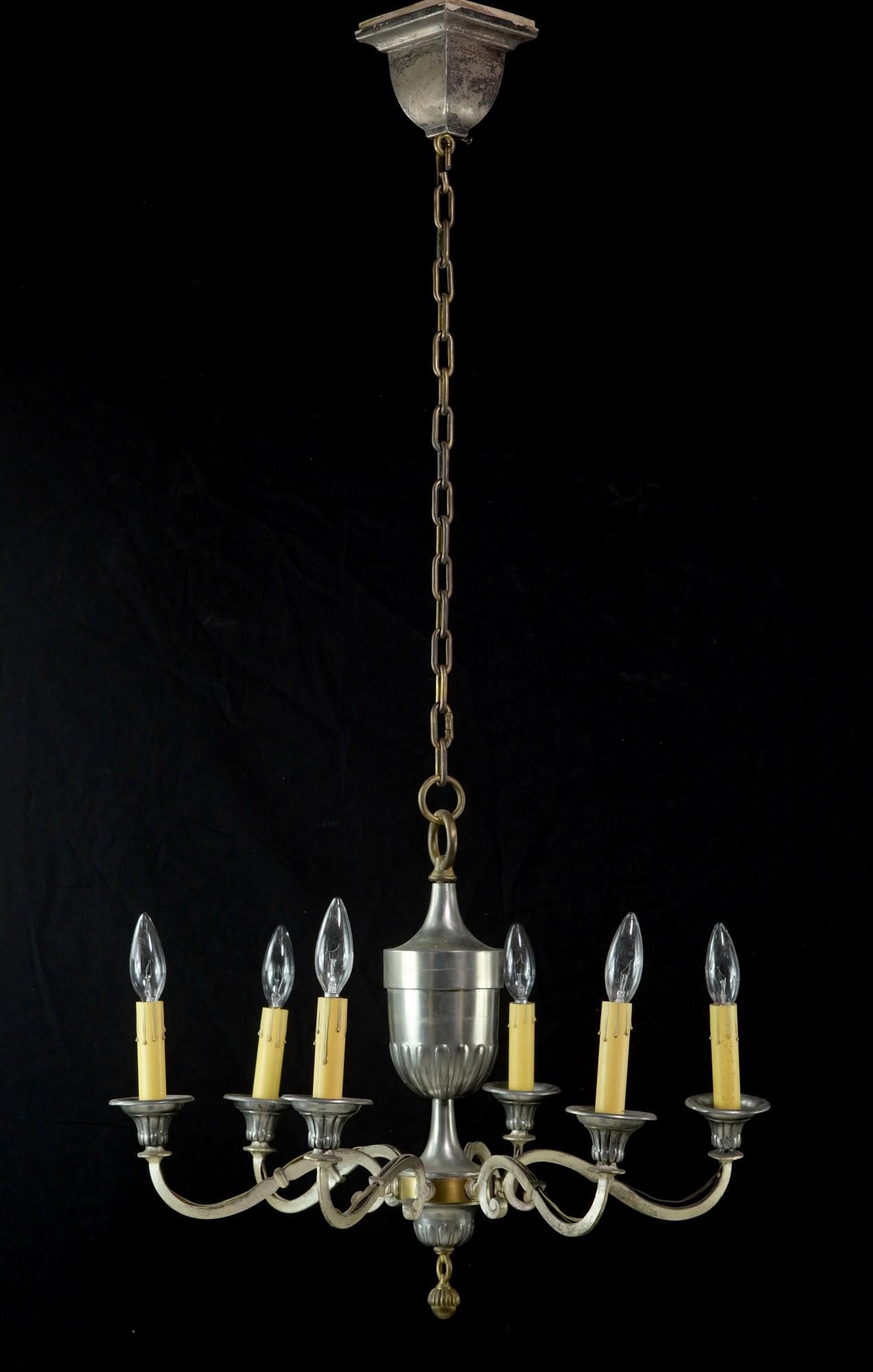 Questo lampadario a 6 luci in stile federale è originale degli anni '40 ed è nichelato su ottone con la patina originale. Ha eleganti bracci che circondano un corpo a forma di urna e presenta un terminale a ghianda. La nichelatura presenta una certa