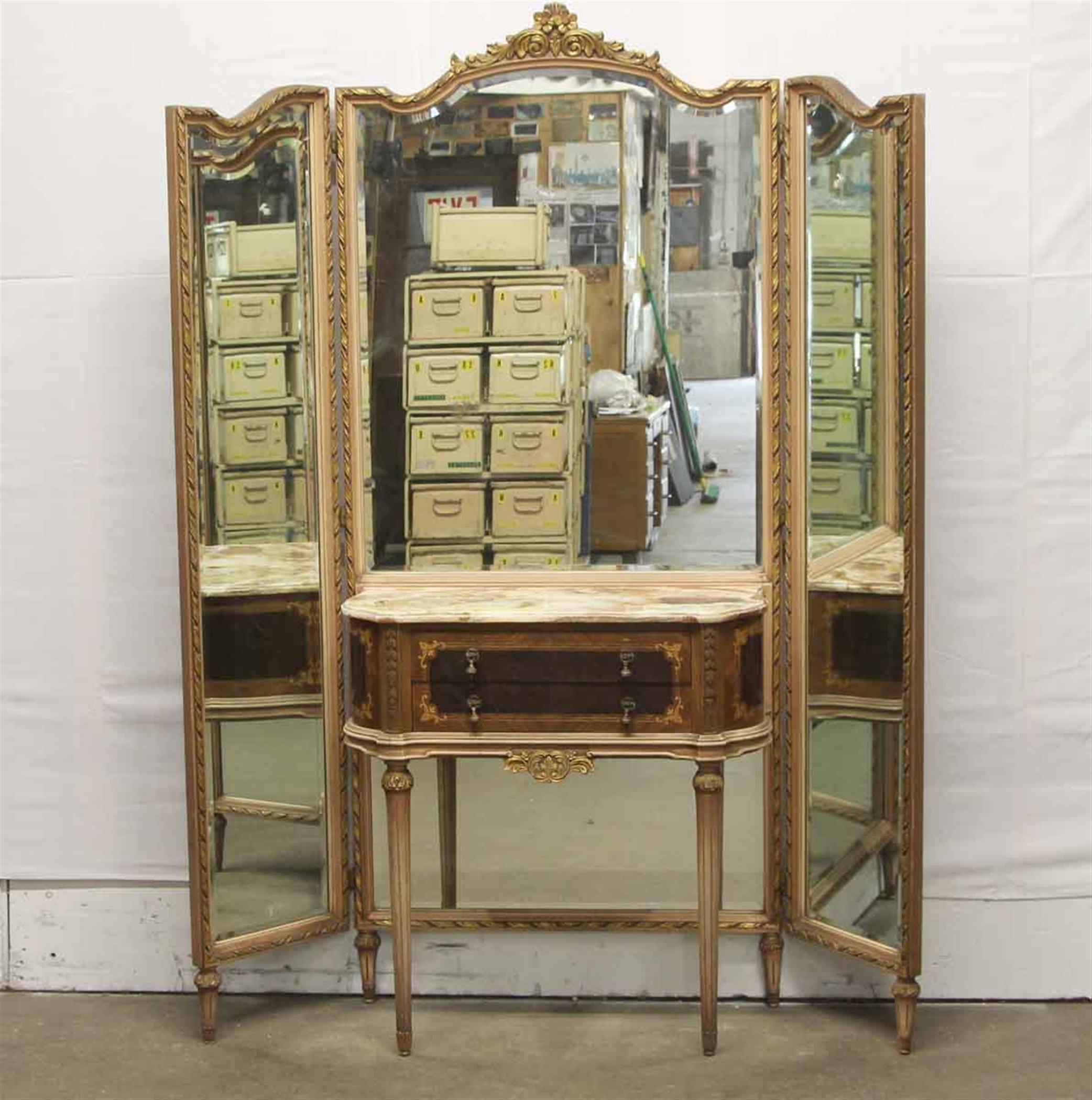 1940s Federal style carved wood entryway table with two drawers and an attached tri-fold mirror. It features a marble top table with brown, gray, yellow and white veining. This can be seen at our 333 West 52nd St location in the Theater District
