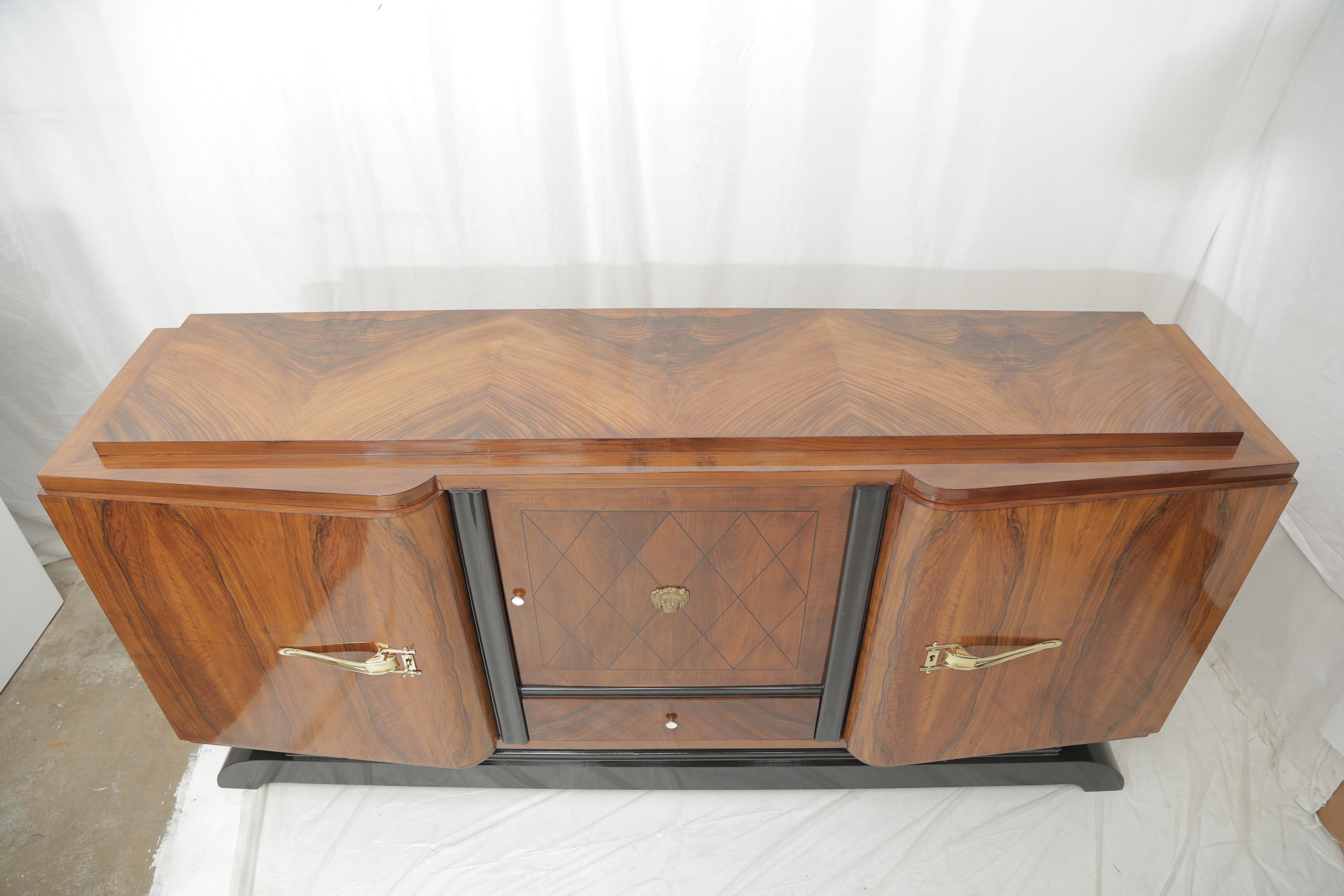 Elegant blond mahogany late Art Deco sideboard with three doors and one central drawer on the lower part, 1940s. Typical curved shapes for the two front doors
Sycamore veneer on the inside of the piece. The central door diamond shape ebony veneer