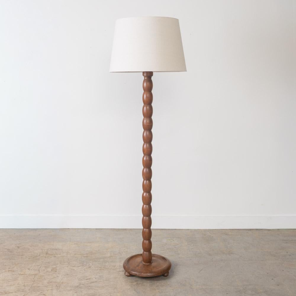 Lovely carved wood floor lamp from France, 1940s. Great carved bobbin stem on a circular base with three ball feet. Original wood finish shows nice age and patina. Newly re-wired and new linen shade. Takes one E26 base bulb, 60 W or higher using