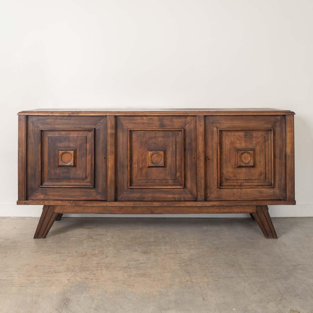 Substantial oak sideboard from France, 1940s. Carved wood square detail on cabinet doors and angular legs. Three doors open to shelves with center drawer for storage. Original dark wood finish shows nice grain in wood with age and patina. Includes