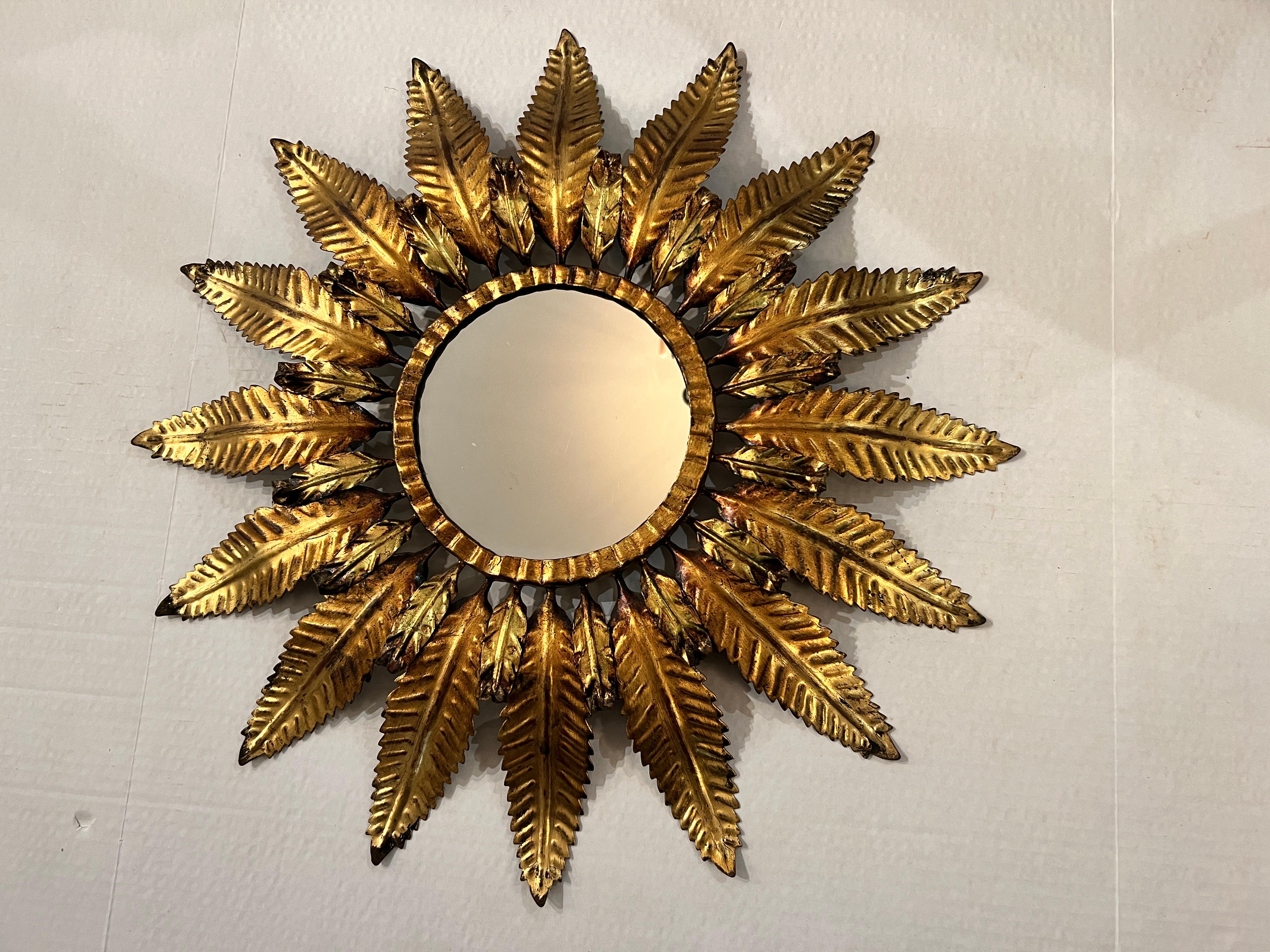 A 1940s French Gilt Metal Sunburst Mirror is a vintage mirror with a radiant design, featuring a sunburst-like frame made of gold-colored metal.
