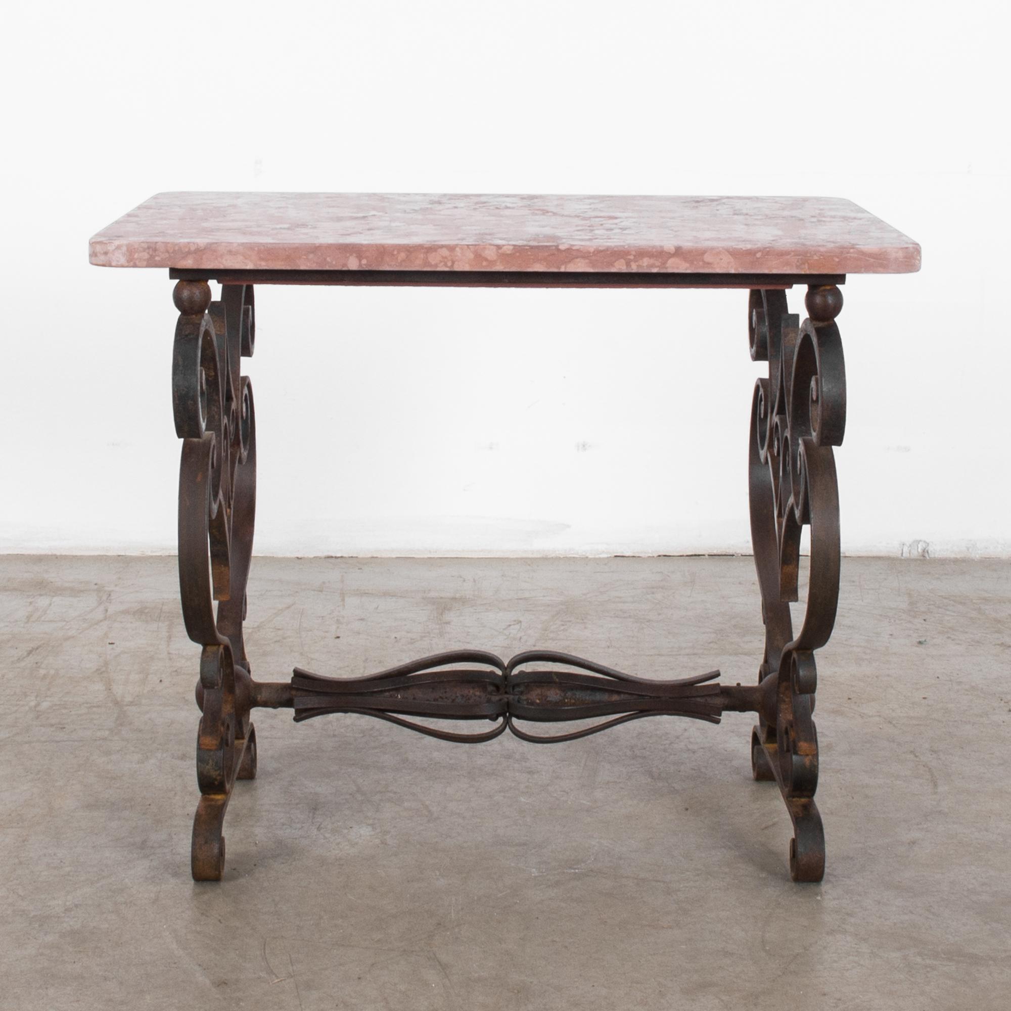 This coffee table was made in France, circa 1940. The rectangular, deep pink marble top rests on an iron frame and presents a stunning accent to any room. The decorative legs feature exquisite scrollwork and flank two whisk-shaped designs on the