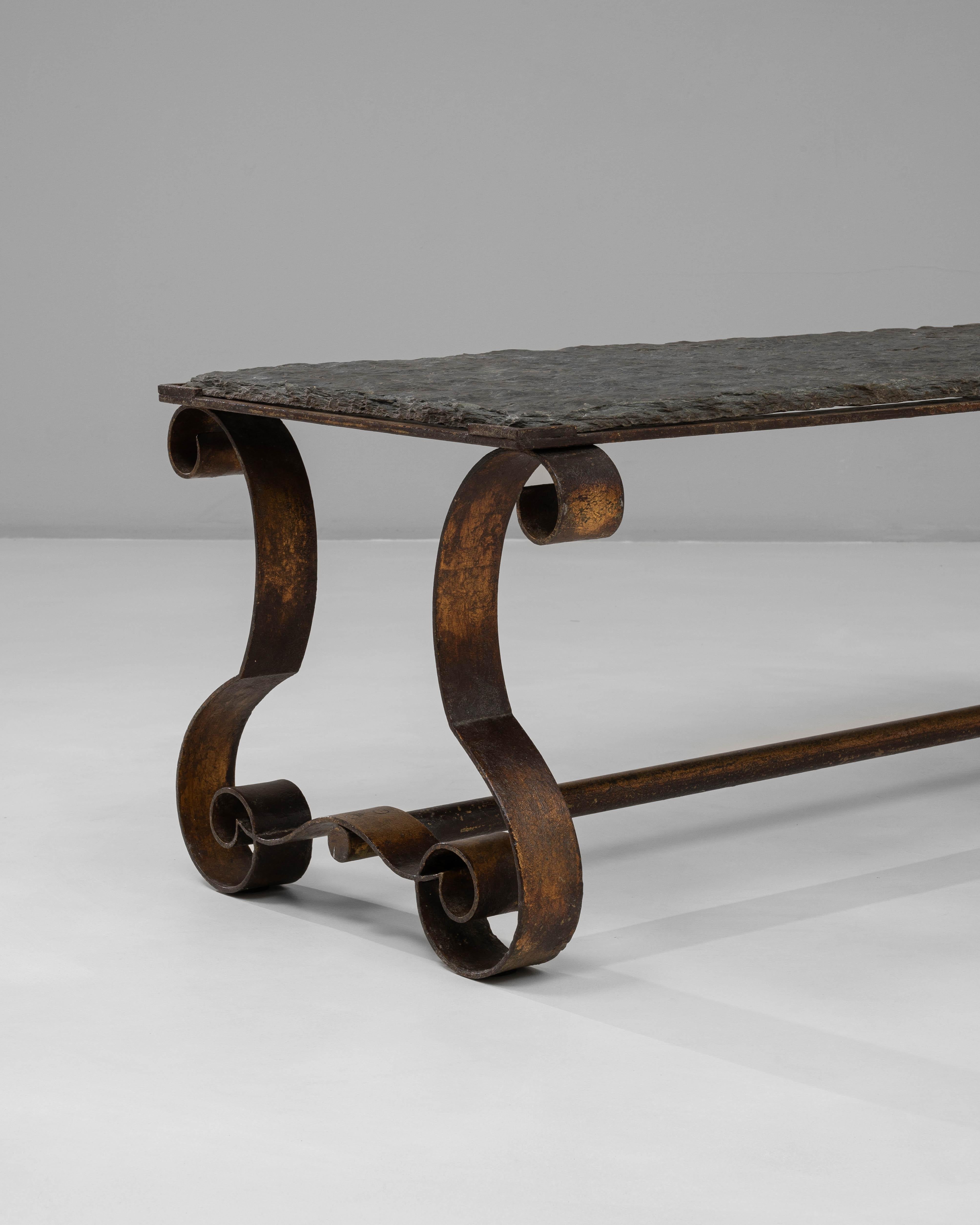 Cette table basse française en métal des années 1940 présente un jeu frappant de formes sculpturales et de matériaux robustes, créant une présence distinctive adaptée à une gamme d'intérieurs. La base en métal forgé à la main est définie par