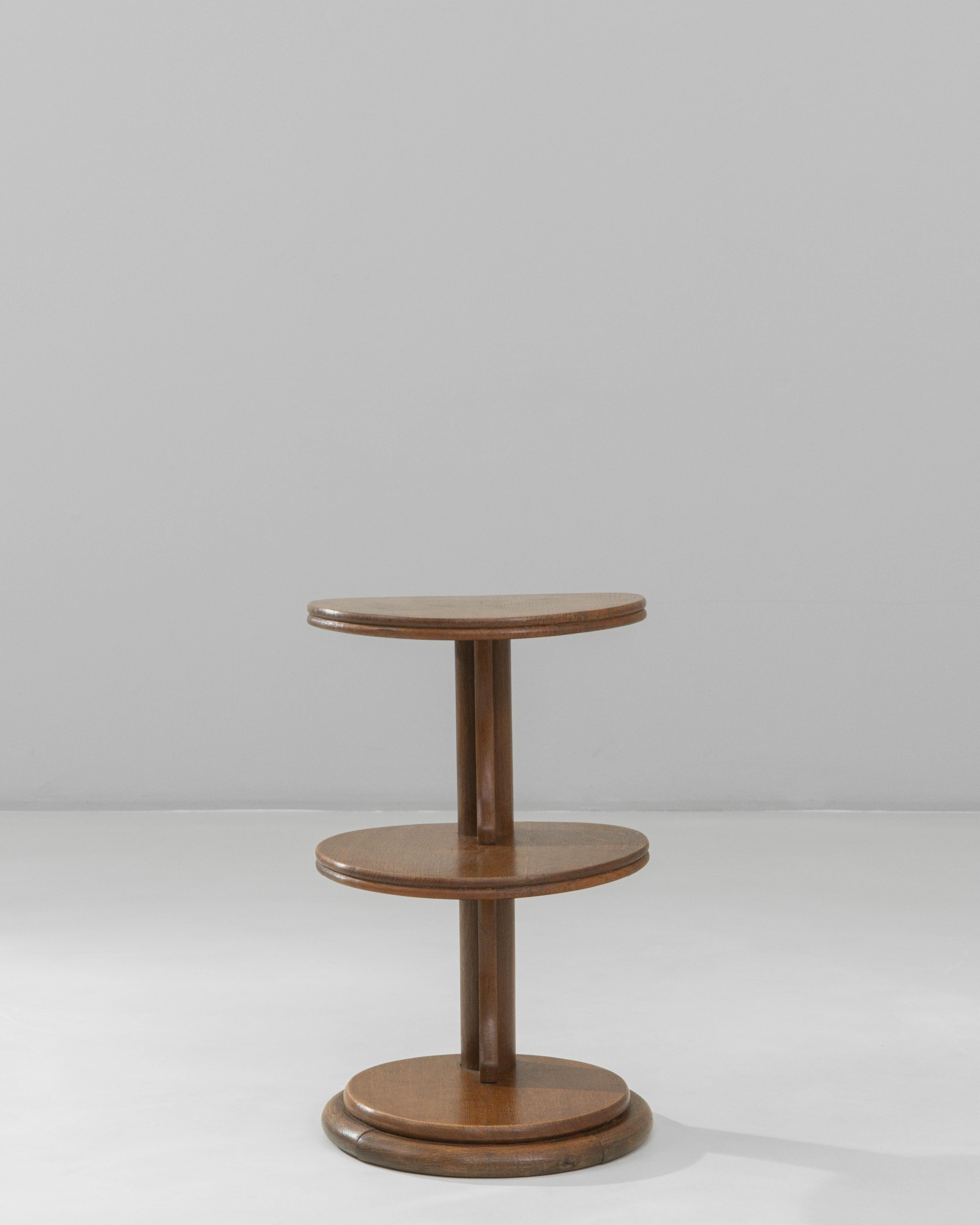 This 1940s French Modern three-tier side table features a clean, architectural silhouette that reflects the era’s shift toward functional design with refined simplicity. Crafted in warm, polished wood, the table is structured around a central column