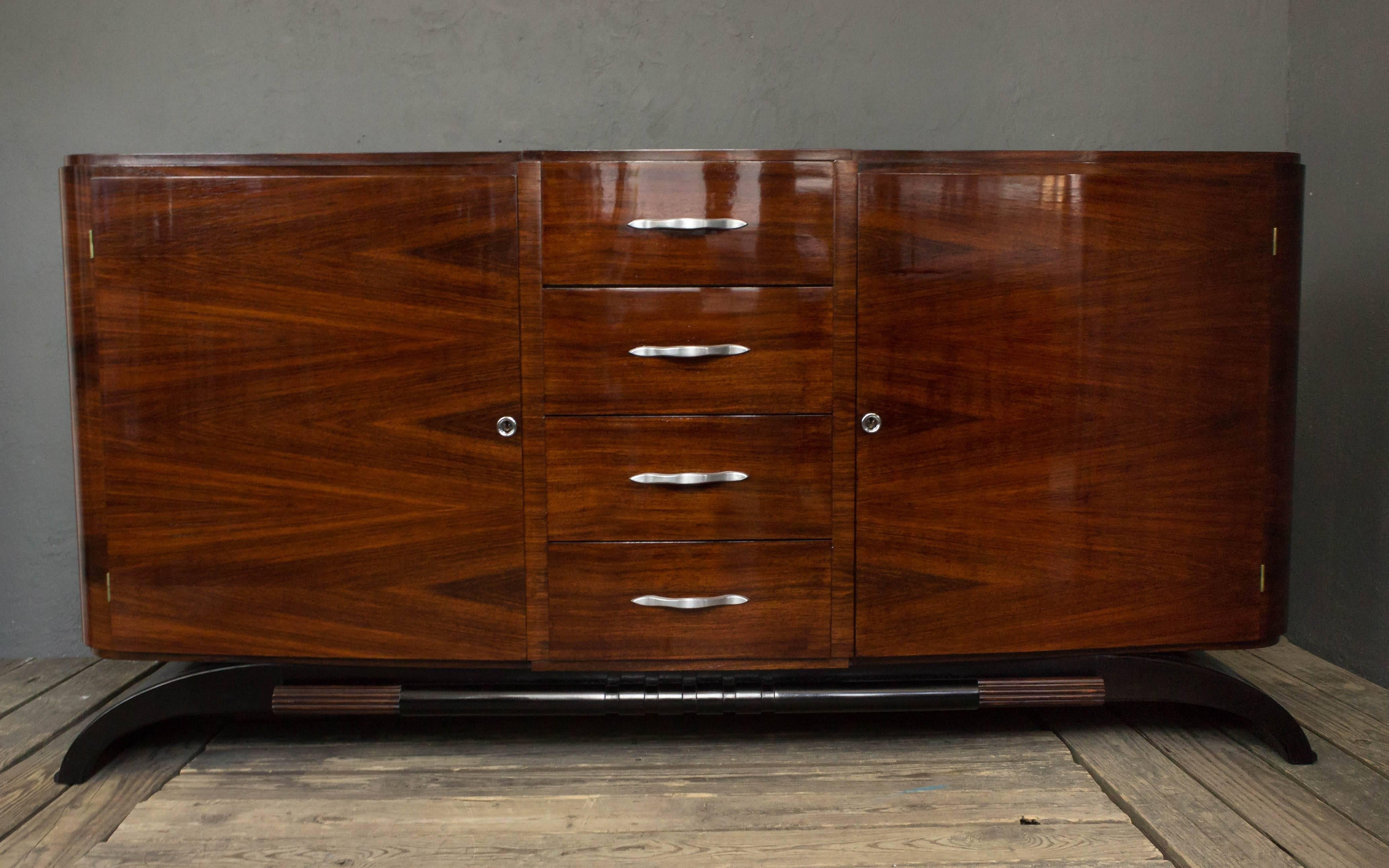 1940s French sideboard with rosewood veneers. Two curved doors reveal 3 adjustable shelves and the sideboard has a center column of drawers with brass hardware. This piece has recently been restored and is in excellent condition.