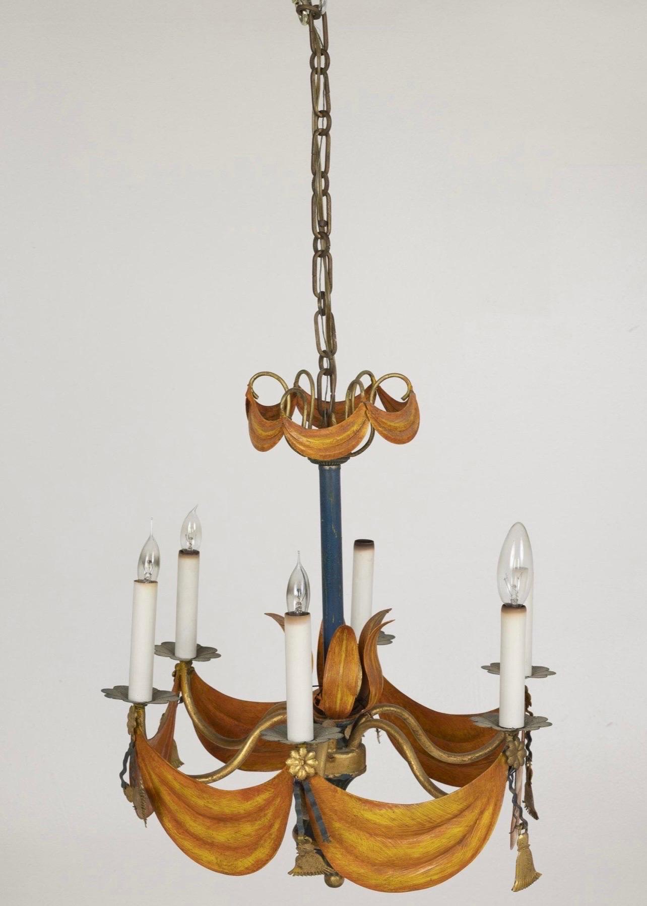 Lustre décoratif Tole à 6 lumières, décoré d'une draperie orange doré en guirlandes et glands sous les chandeliers se terminant par un fleuron en forme de boule.  C. 1940's
Dimensions : Hauteur : 19 1/2 po. x Largeur : 18 1/2 po.