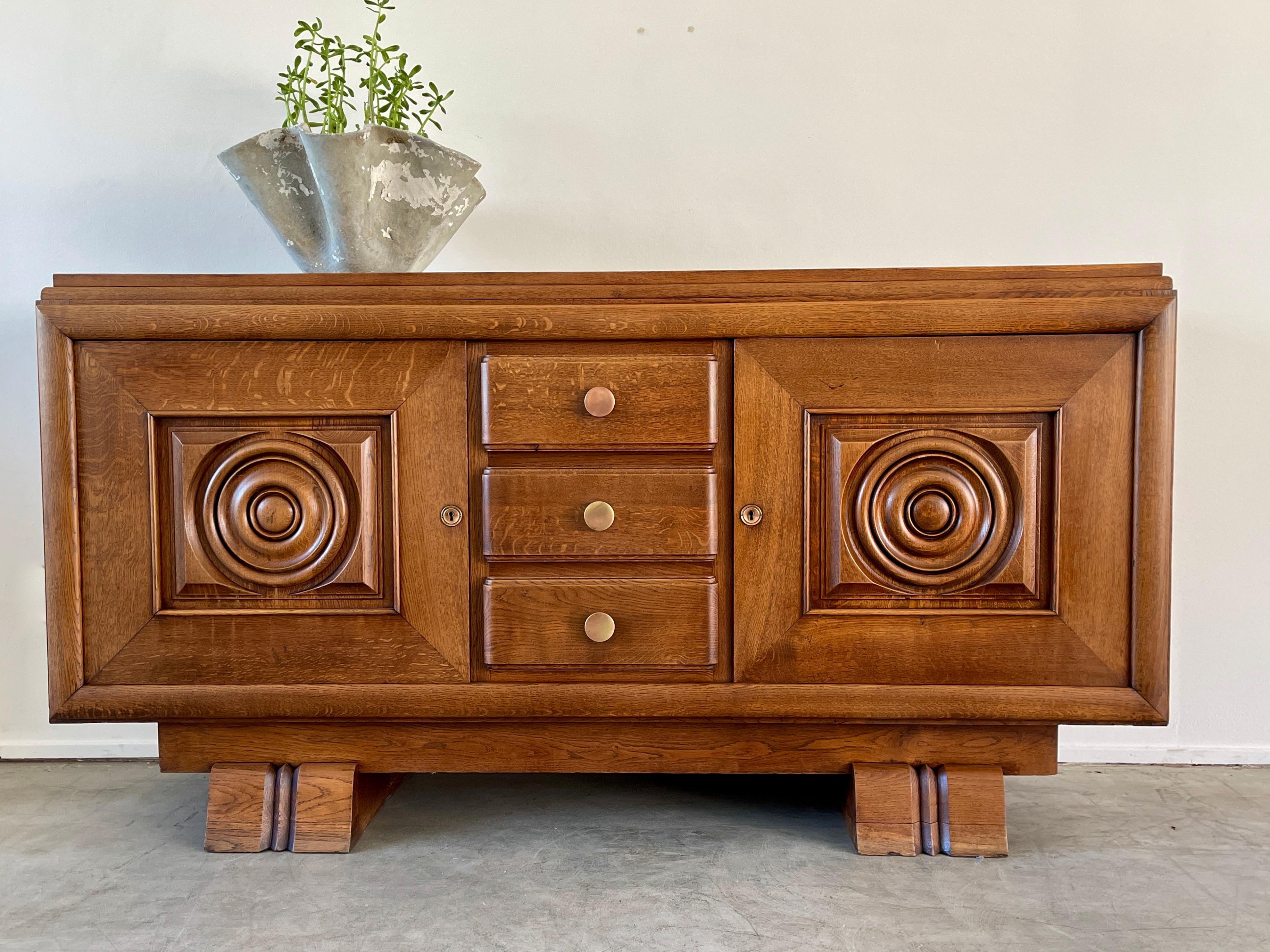 1930's French walnut cabinet with concentric circle carvings on each door and ornate detail throughout. 
Original brass hardware - open shelving on each side with center drawers in center
Gorgeous original patina.