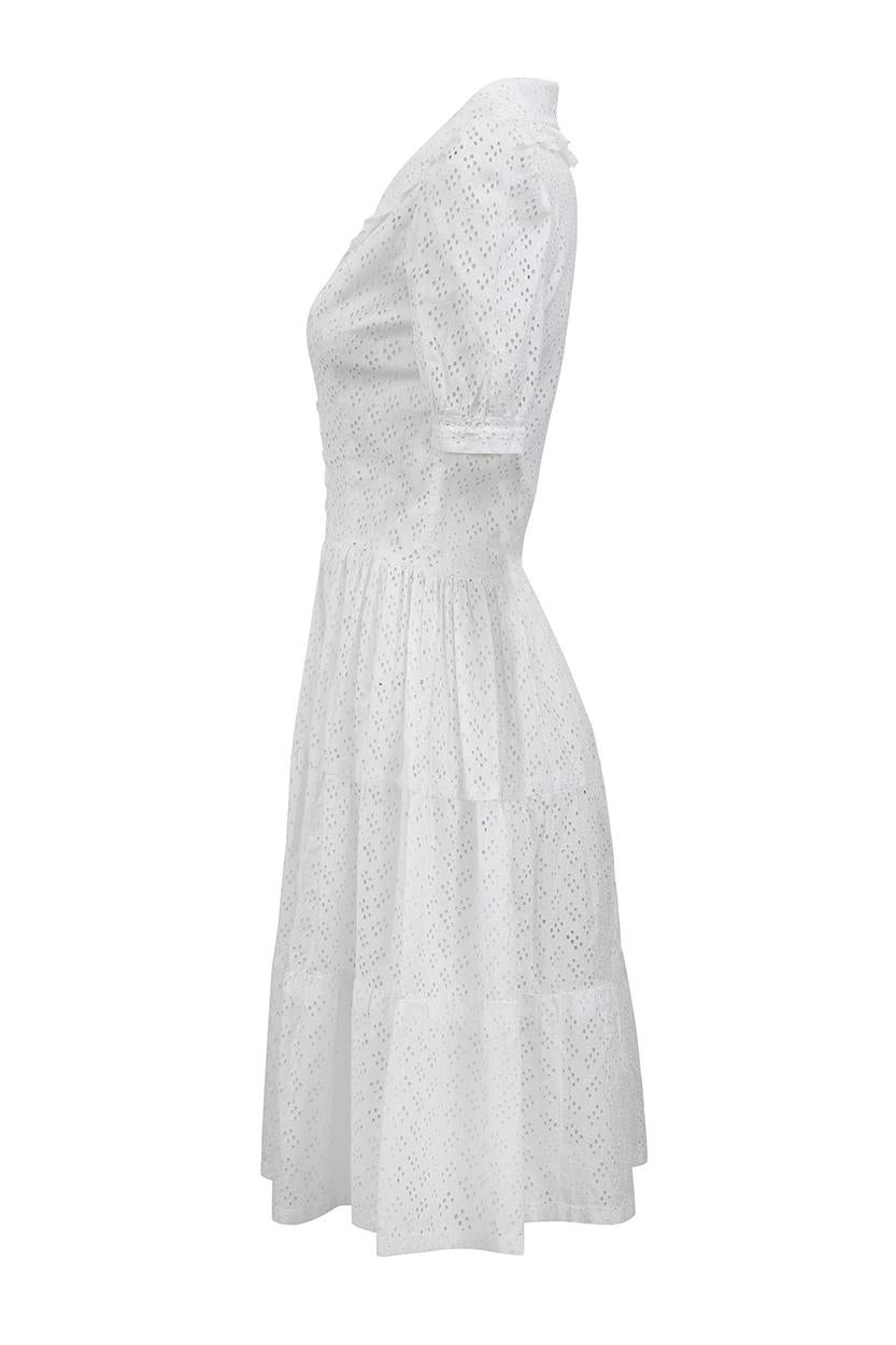 This charming late 1940s white cotton dress has been hand made with exceptional skill and has some exquisite details. It is comprised of white cotton fabric featuring machined eyelet work of geometric clusters arranged to create an alternating