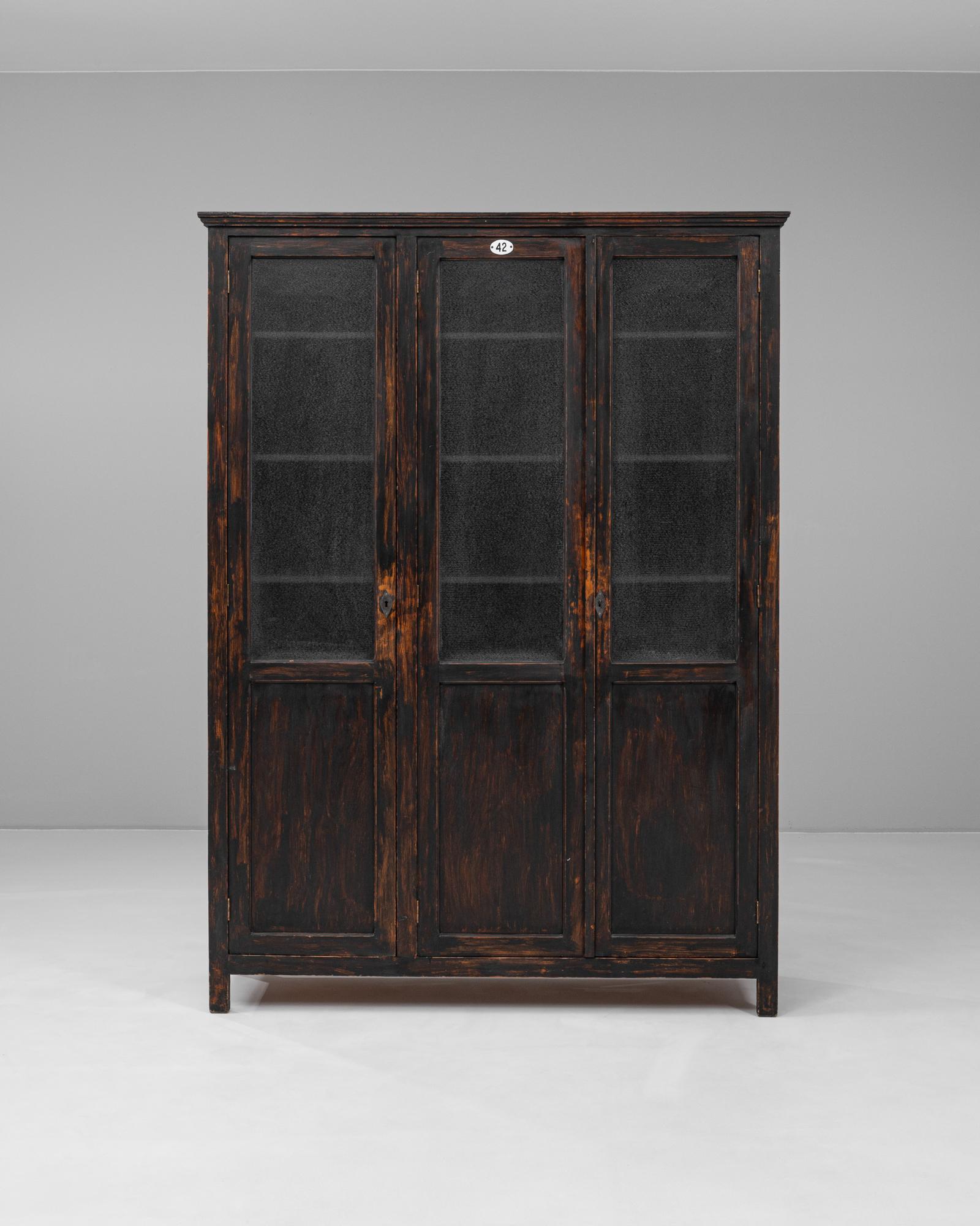 Diese französische Vitrine aus den 1940er Jahren besticht durch ihre schwarz patinierte Oberfläche, die ihre architektonische Form und ihre zweckmäßige Eleganz unterstreicht. Der aus Holz gefertigte Schrank verfügt über drei hohe Glastüren mit