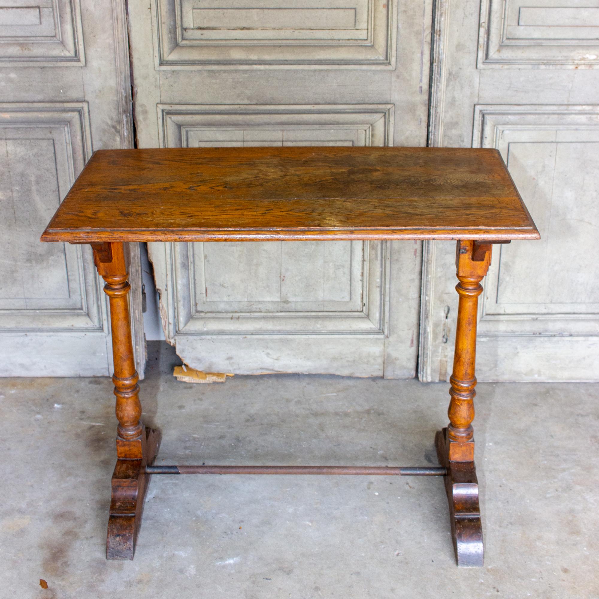 This charming 1940s French bistro table is crafted in wood and metal. The majority of the piece is wood with a brass stretcher at the base between the legs. The legs feature turned details and the rectangular top has a decorative edge. The shape and
