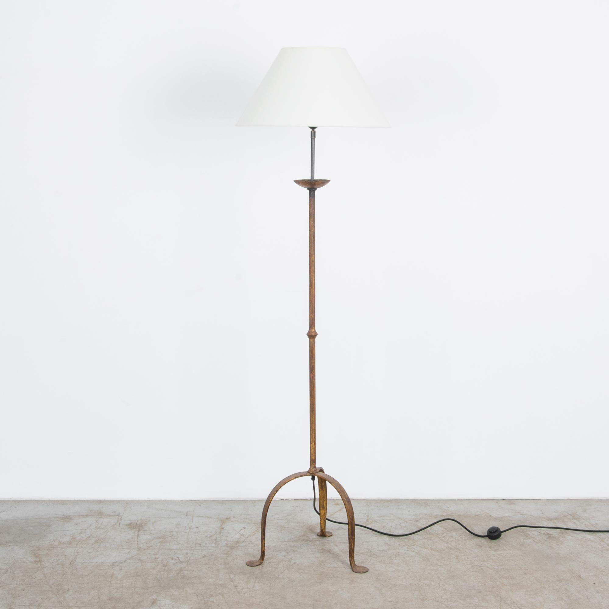 From France circa 1940, this wrought iron lamp captures the traditional forms of hand forged iron, seen through a Modernist lens. This rustic floor lamp rests on playful anthropomorphic feet, updated with contemporary electrical wiring. Aged gold
