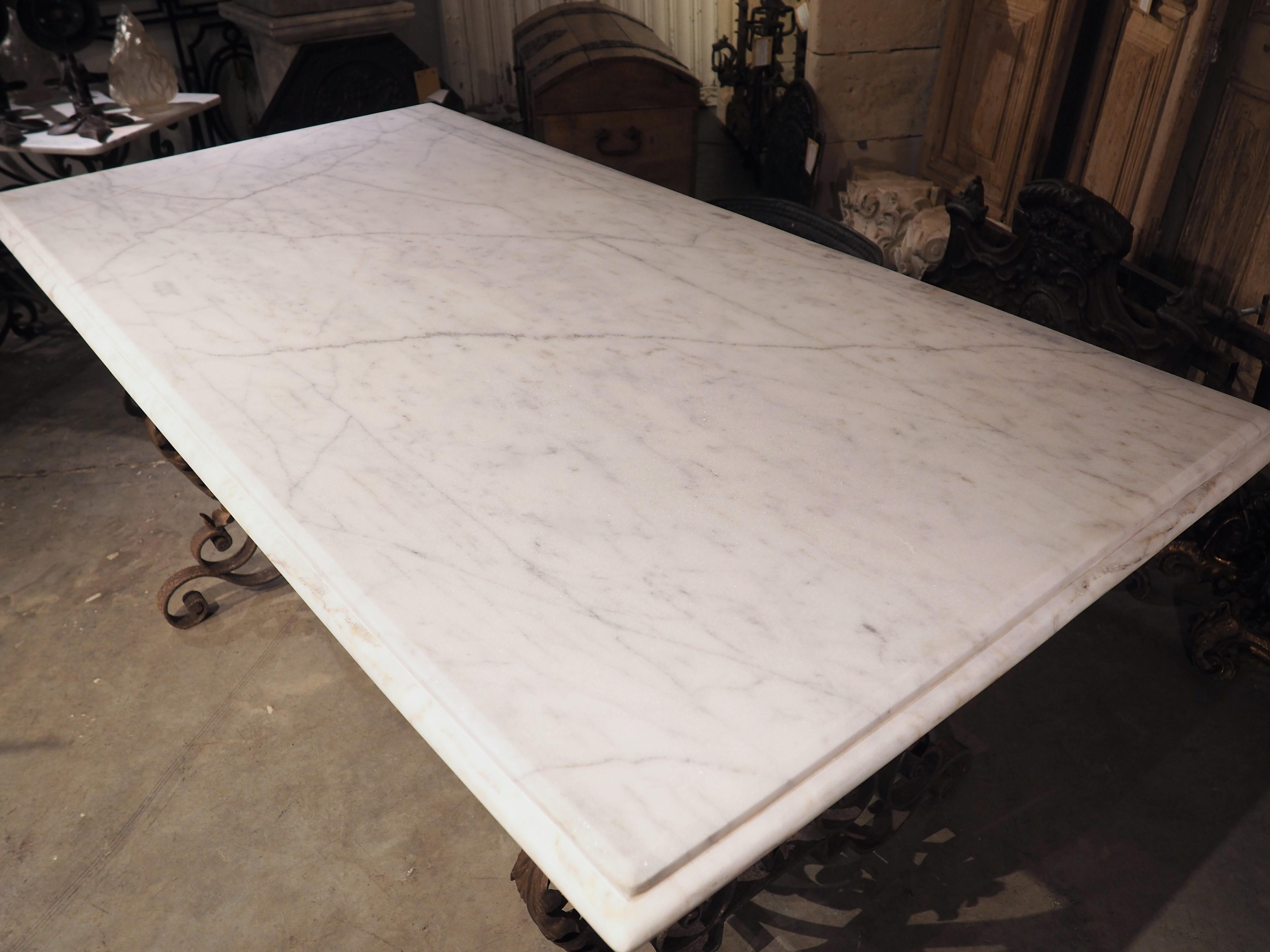 A luxurious marble top with recessed quarter round molding tops a highly scrolled wrought iron base on this French table from the 1940’s. The white Carrara marble has dark gray veining, while the iron base, which features a speckled rust/brown