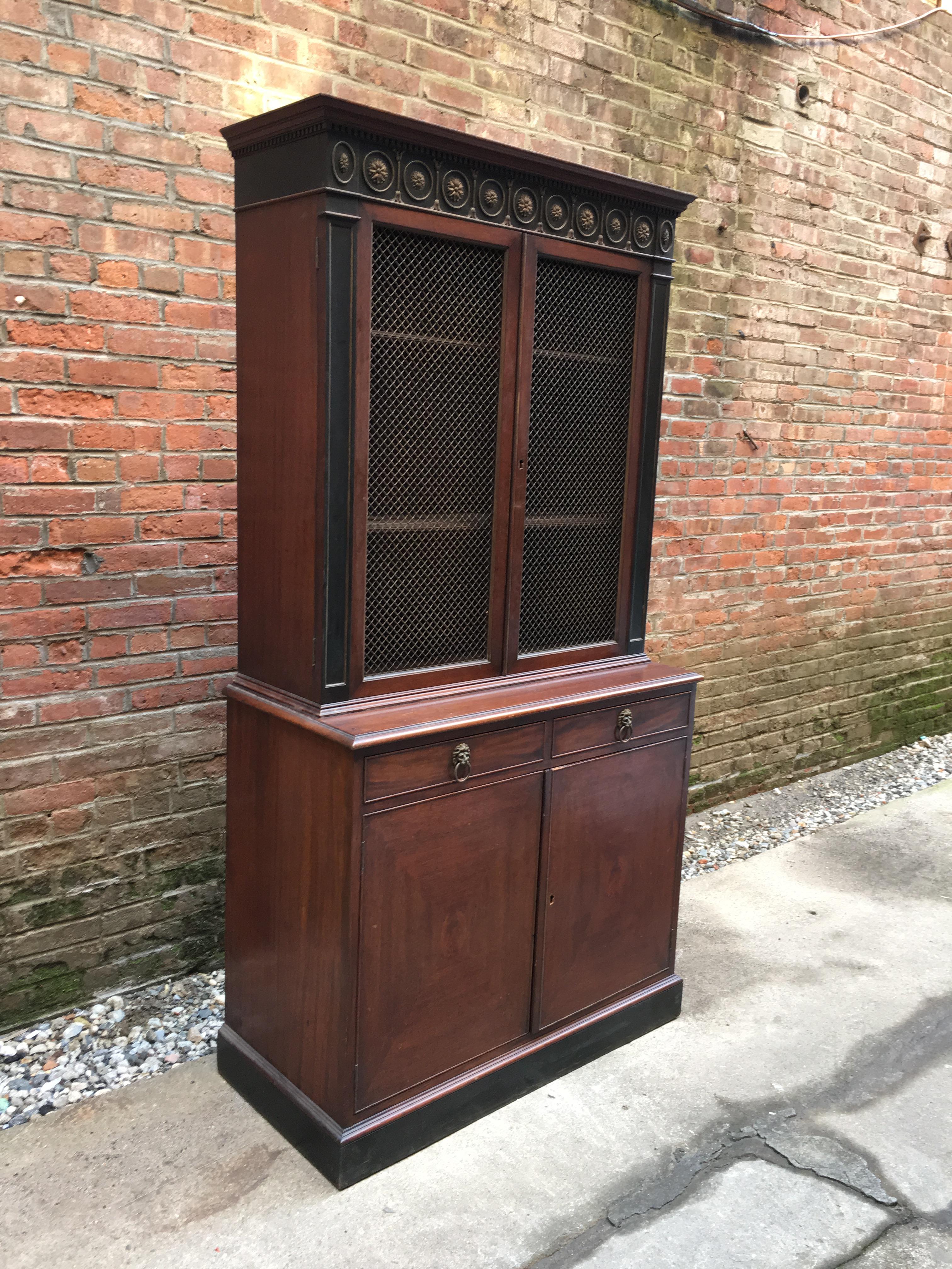 Two-piece mahogany cabinet with great attention to detail. This piece features metal grill work and interior shelves; three adjustable shelves in the upper case and one larger adjustable shelf in the bottom case. The wonderful pediment features a