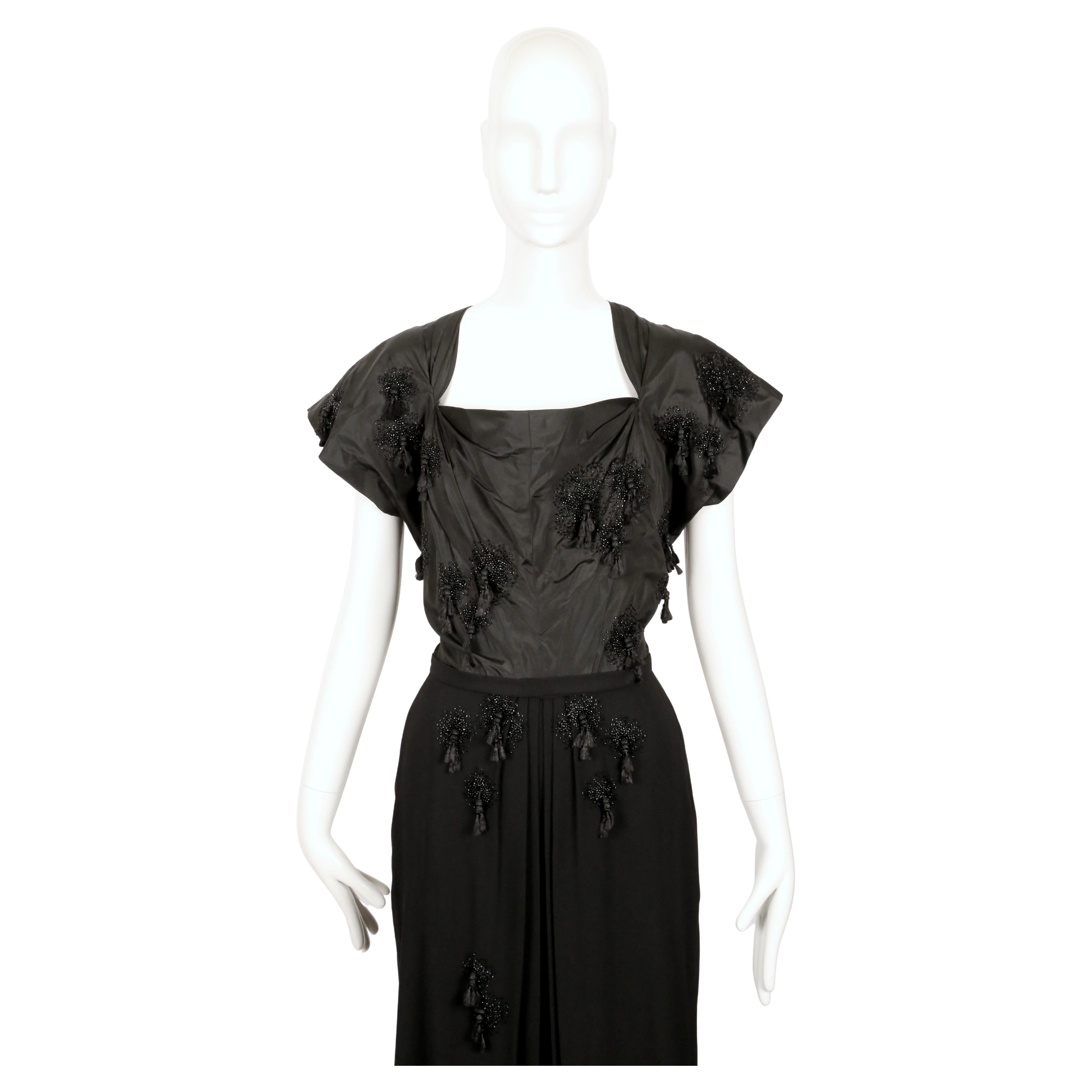 Striking black cocktail dress created by Hollywood costume designer Gilbert Adrian which exemplifies his unique use of sharp structure and ornamentation.  This dress dates to the 1940's.  

The bodice of the dress is made from crisp black silk