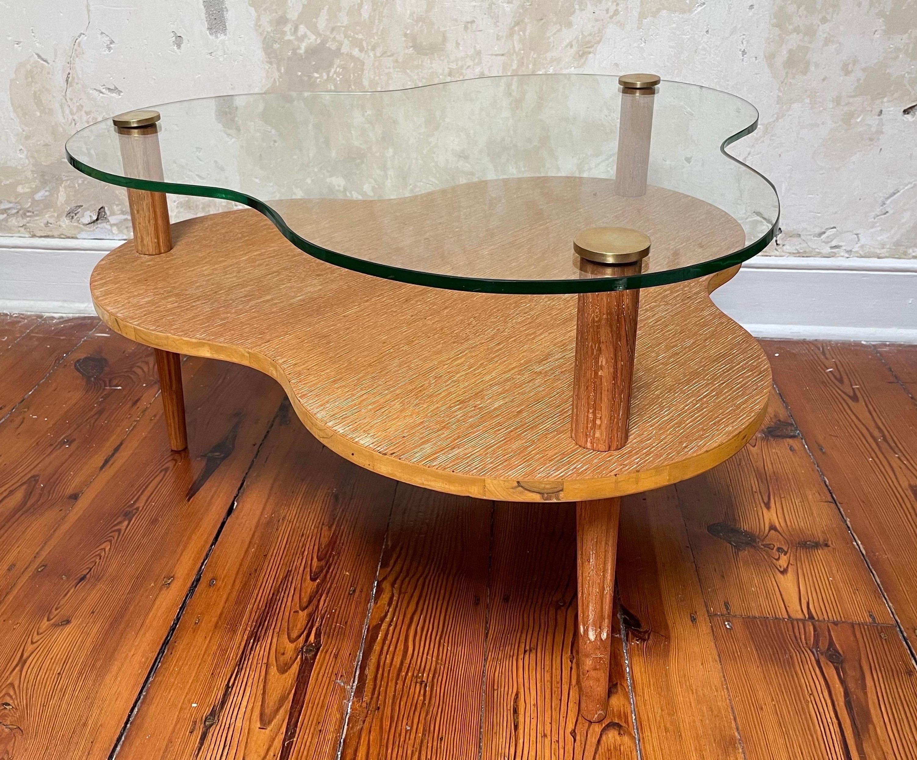 A glass and cerused oak 2 tier cloud shaped coffee table (or oversized accent table) with carved tripod legs and brass caps. Designed by Gilbert Rhode for Herman Miller for the early 1940s Paldao Group. The forms and materials of this line paid