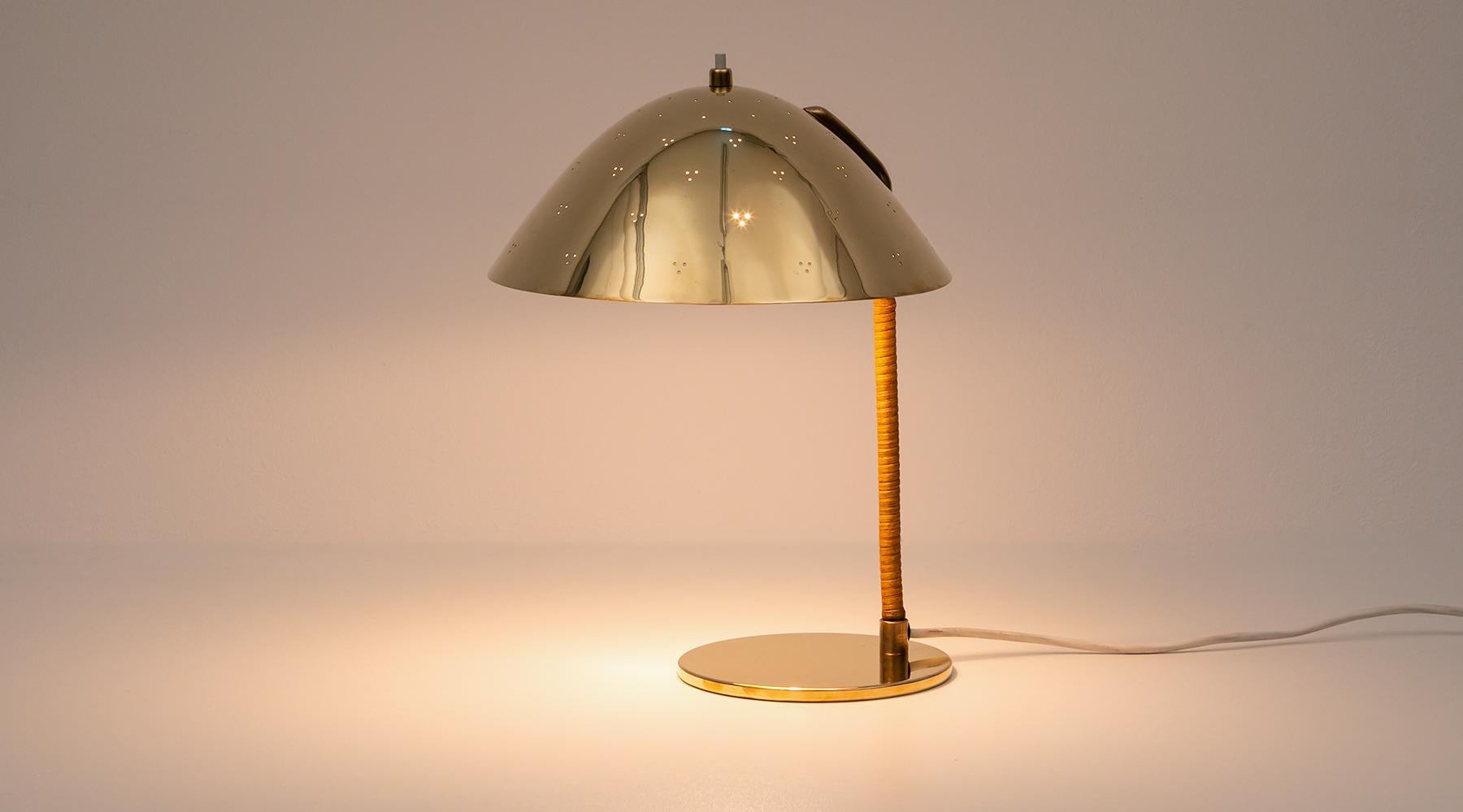 Rare and lovely table lamp designed by famous Paavo Tynell. The shade is in brass and decorated with perforation. The stem comes covered by cane and ends in a round brass feet. Manufactured by Taito Oy. 

Tynell was one of the founders of Taito