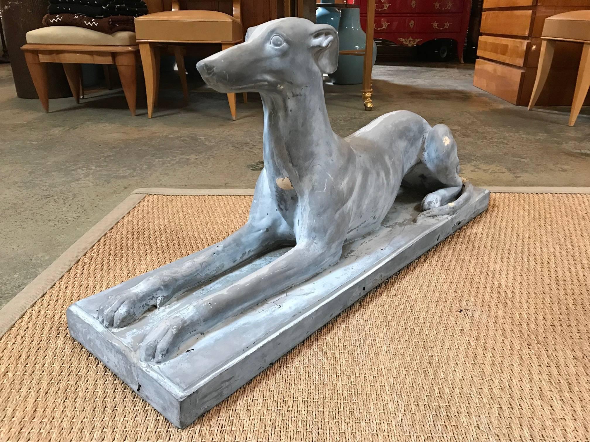 Laying Whippet dog with upright posture molded in composition material.