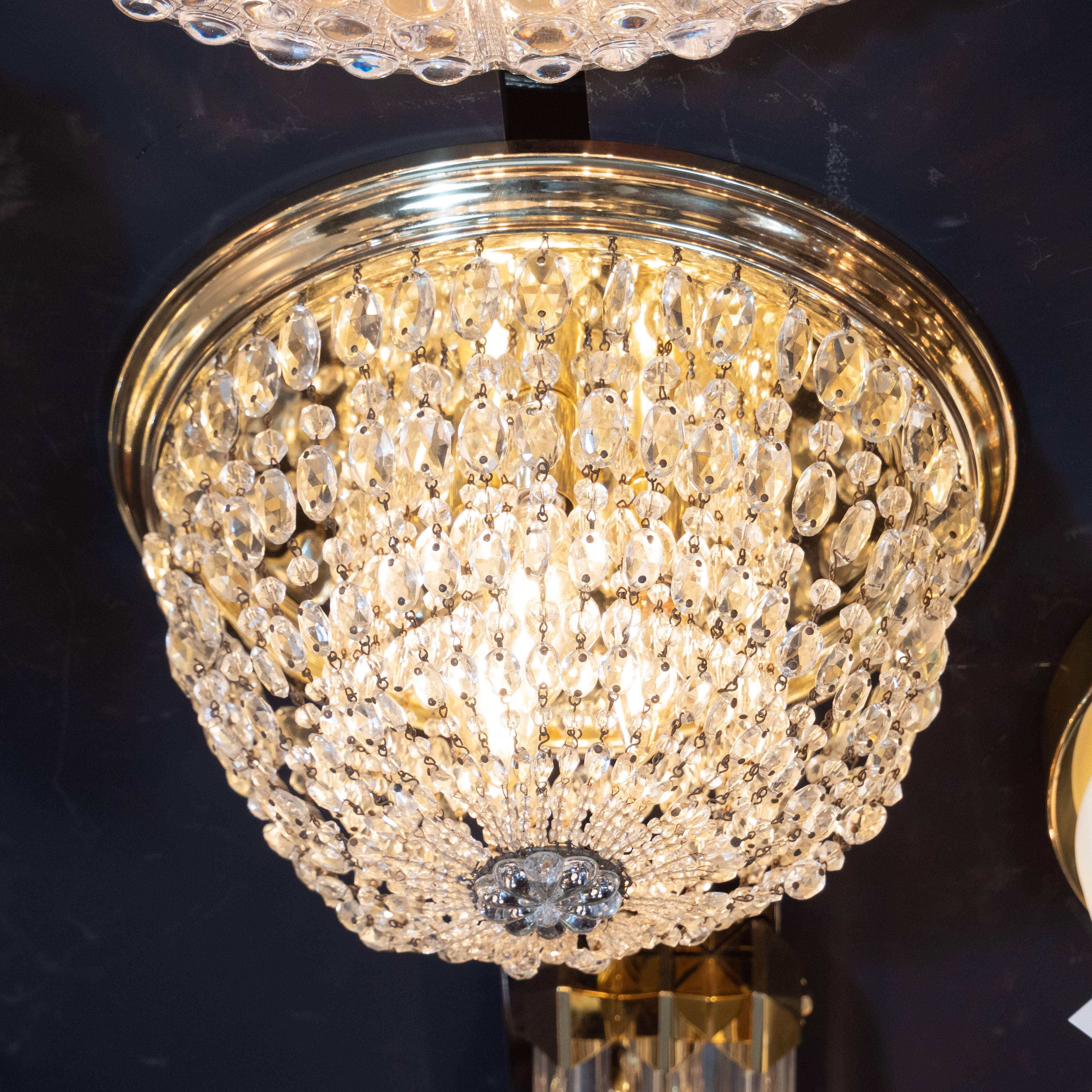 This glamorous and elegant Hollywood flush mount was realized in the United States, circa 1945. It features a stepped skyscraper style brass base from which an abundance of strands of cut crystal elegantly drape downwards, secured in the center of