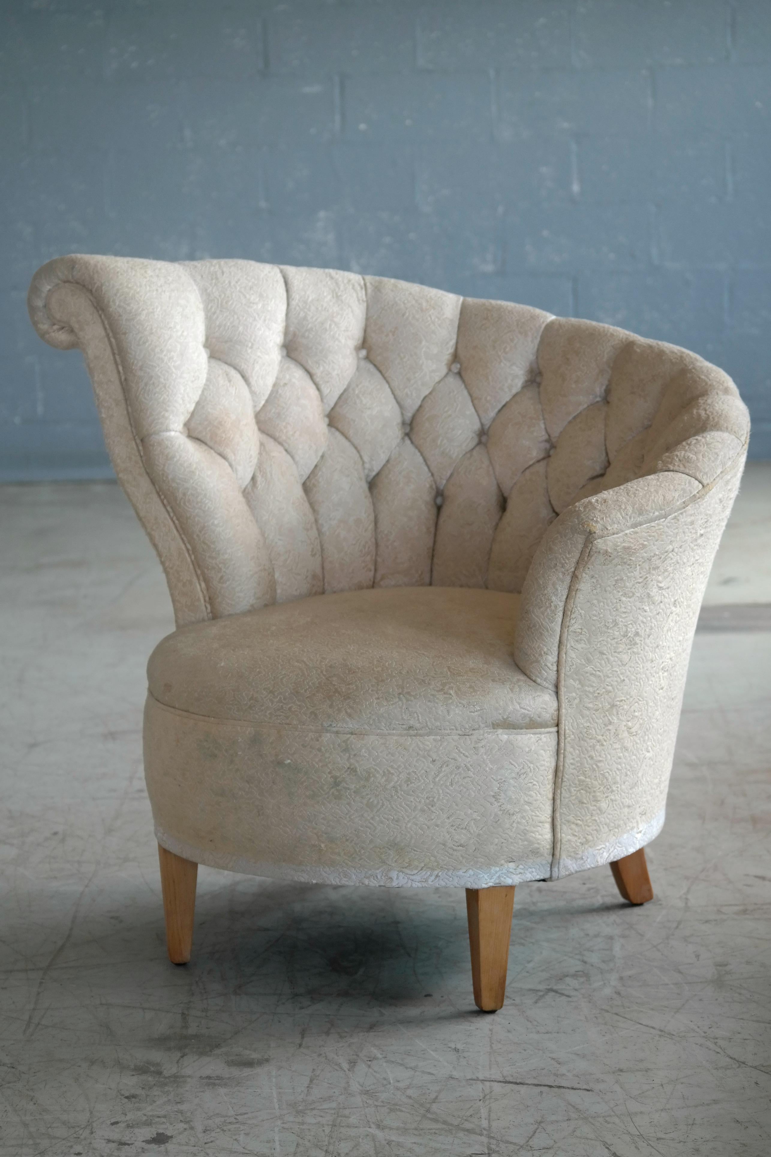 Whimsical and glamorous 1940s Hollywood Regency style lounge chair. The chair have a circular design when seen from above and the back feature an asymmetrical fan back design with tufted upholstery and a slight scroll detail on the highest point.