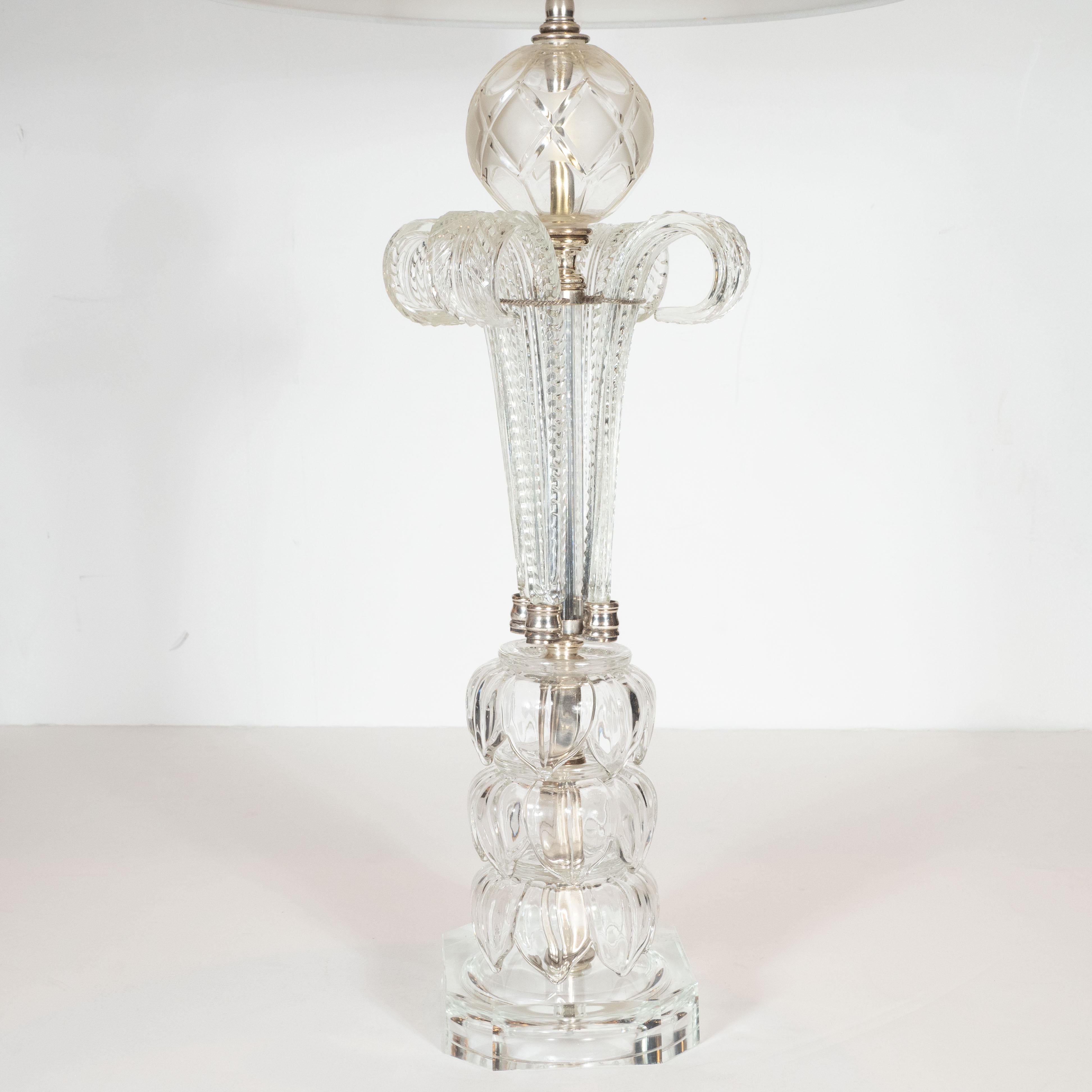 This exquisite Hollywood Regency table lamp was realized in the United States, circa 1940. It features three stacked volumetric ovoid forms with etched foliate detailing atop an elongated octagonal base from which ascends four stylized curling