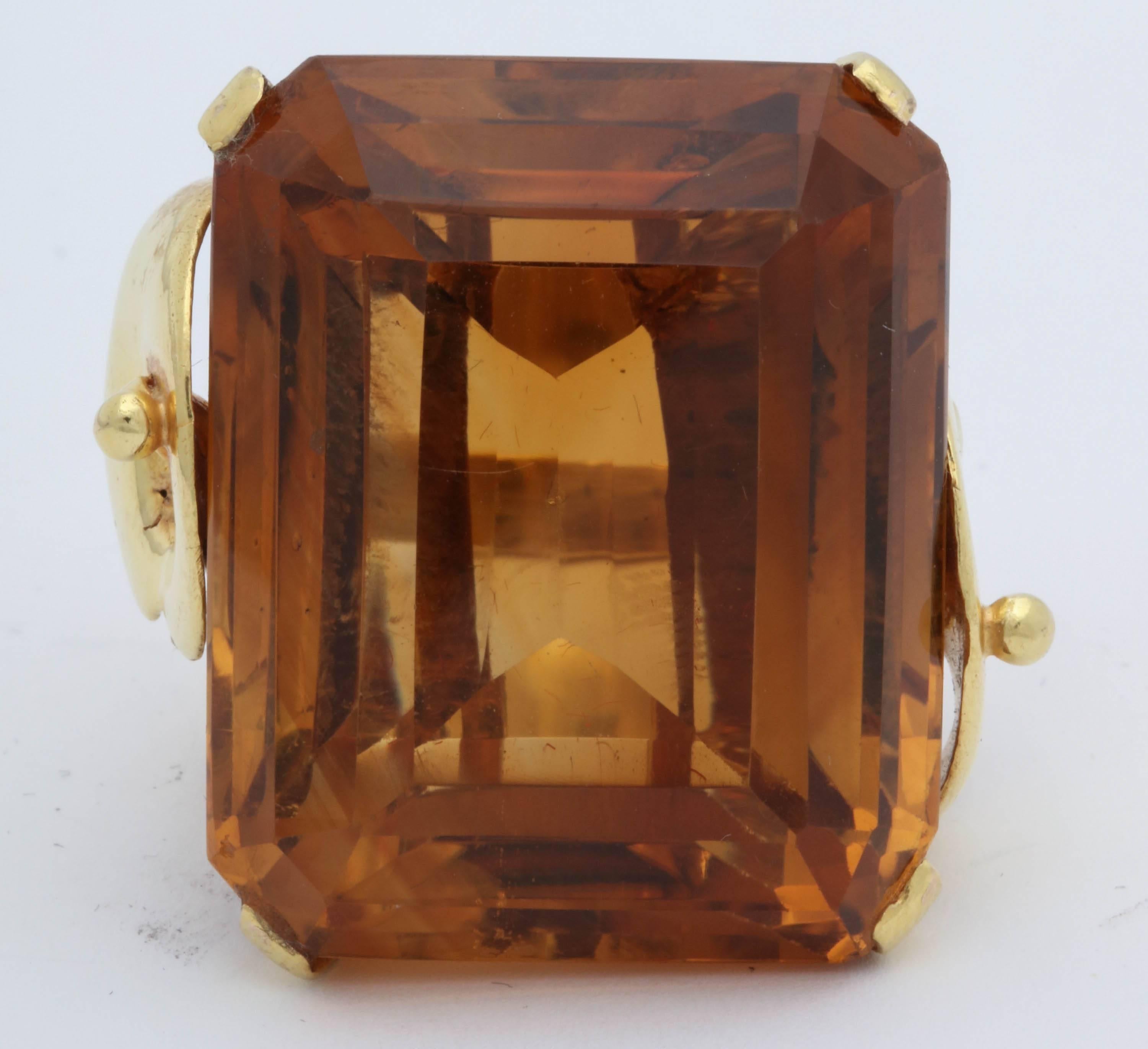 One Ladies Large And Dramatic Emerald Cut Deep Honey Colored Madeira Topaz{Citrine} Weighing Approximately 65 Carats. Large Citrine Is Beautifully Set In a Handmade Sculptural Mounting Made Of 18kt Yellow Gold.NOTE: RING Currently Size 6.5 May