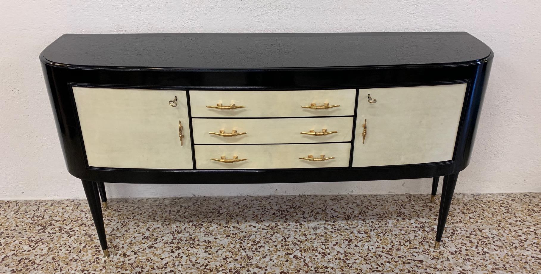 This sideboard was produced in the 1940s in Italy.
Two doors and three drawers are covered in parchment while the structure is black lacquered.
The handles are in brass while the top is in black glass.