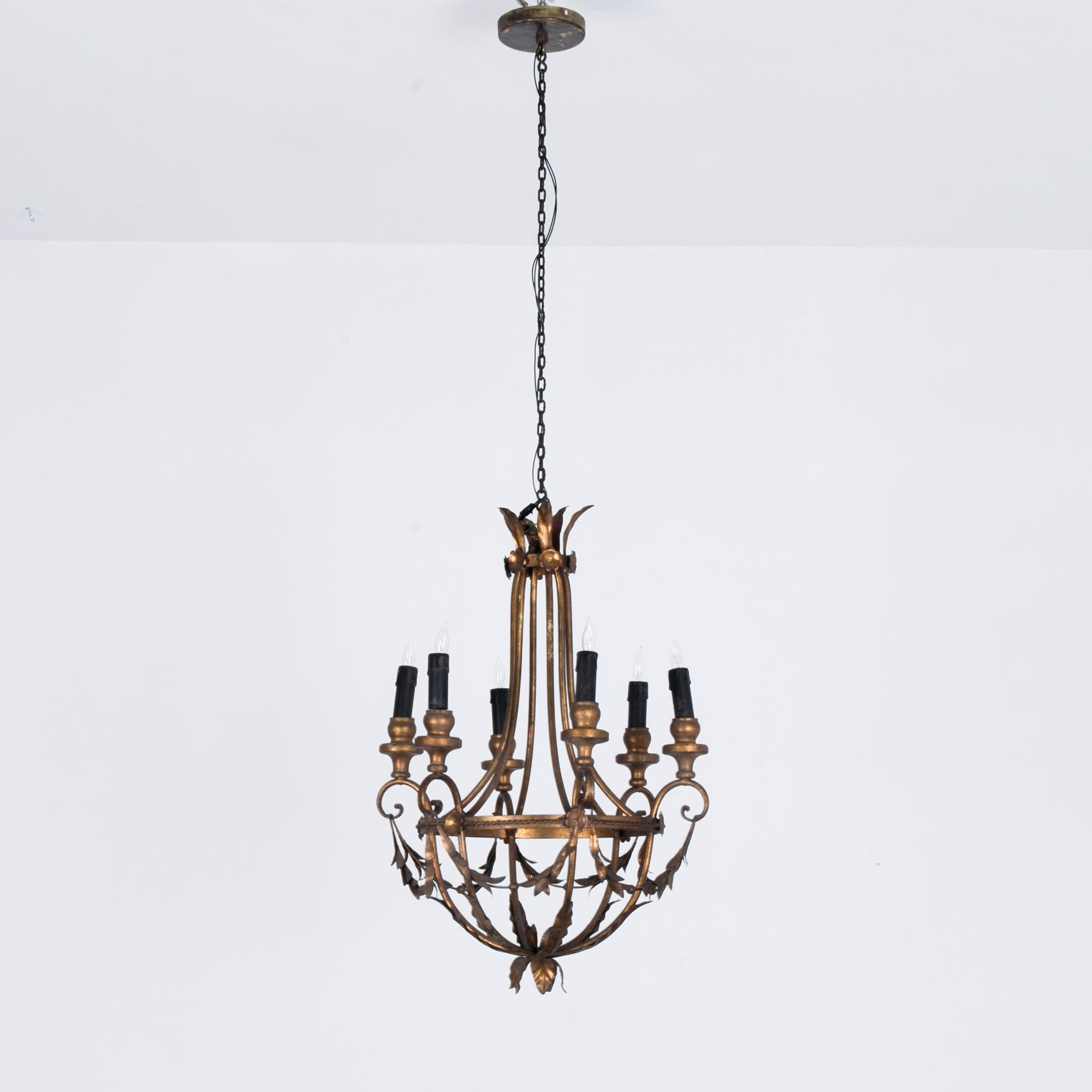 A gilded chandelier from Italy, circa 1940. An elaborate Rococo pendant supports six candelabra bulbs. Garlands of golden leaves hang in loose festoons. The gilded finish of the metal has aged into a warm bronze tone, flattering the fine adornment.