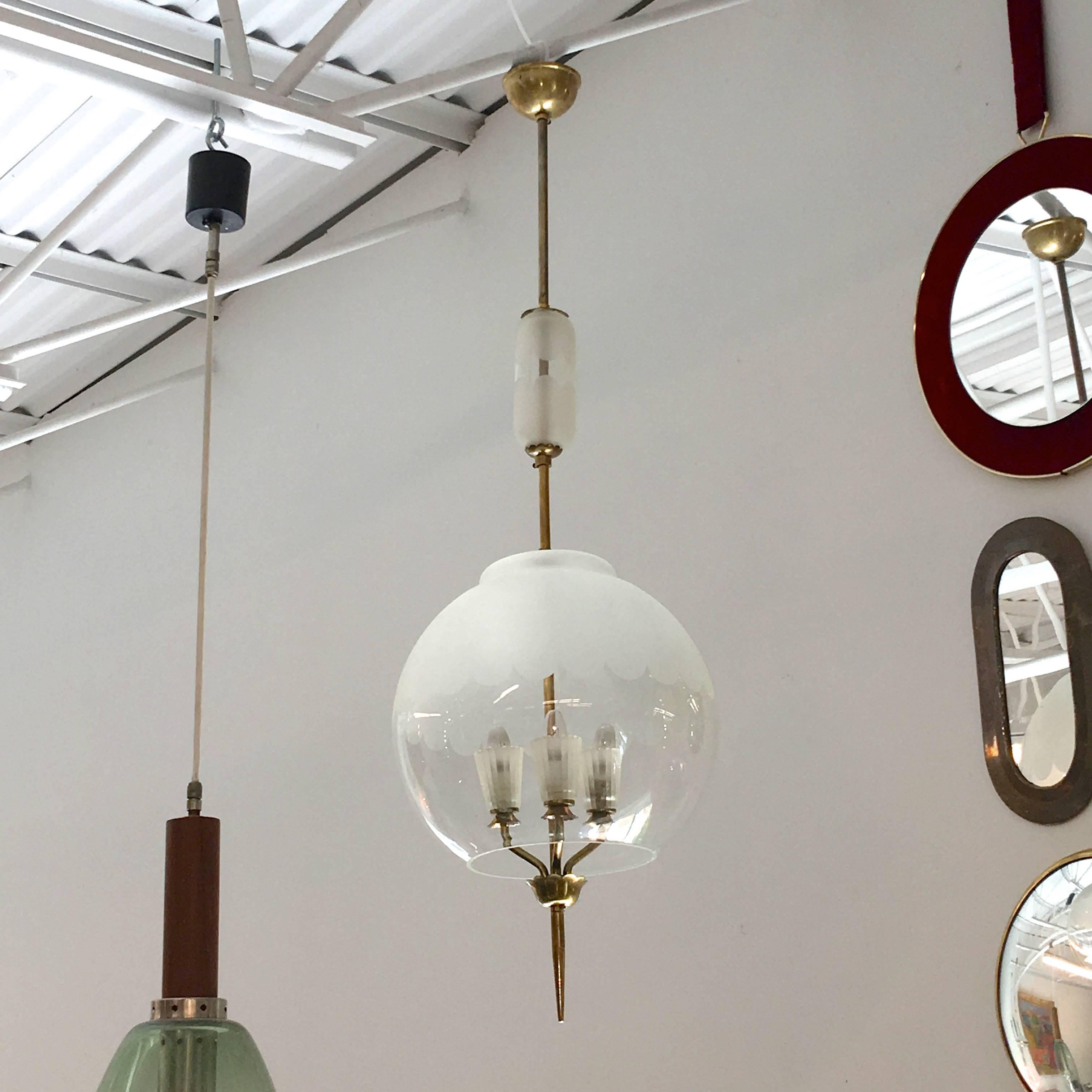 1940s Italian pendant in the manner of Pietro Chiesa for Fontana Arte. A round glass orb with frosted design on upper hemisphere, seemingly floats suspended over brass candle cluster with three lights in frosted glass cups, embellished by a tapered