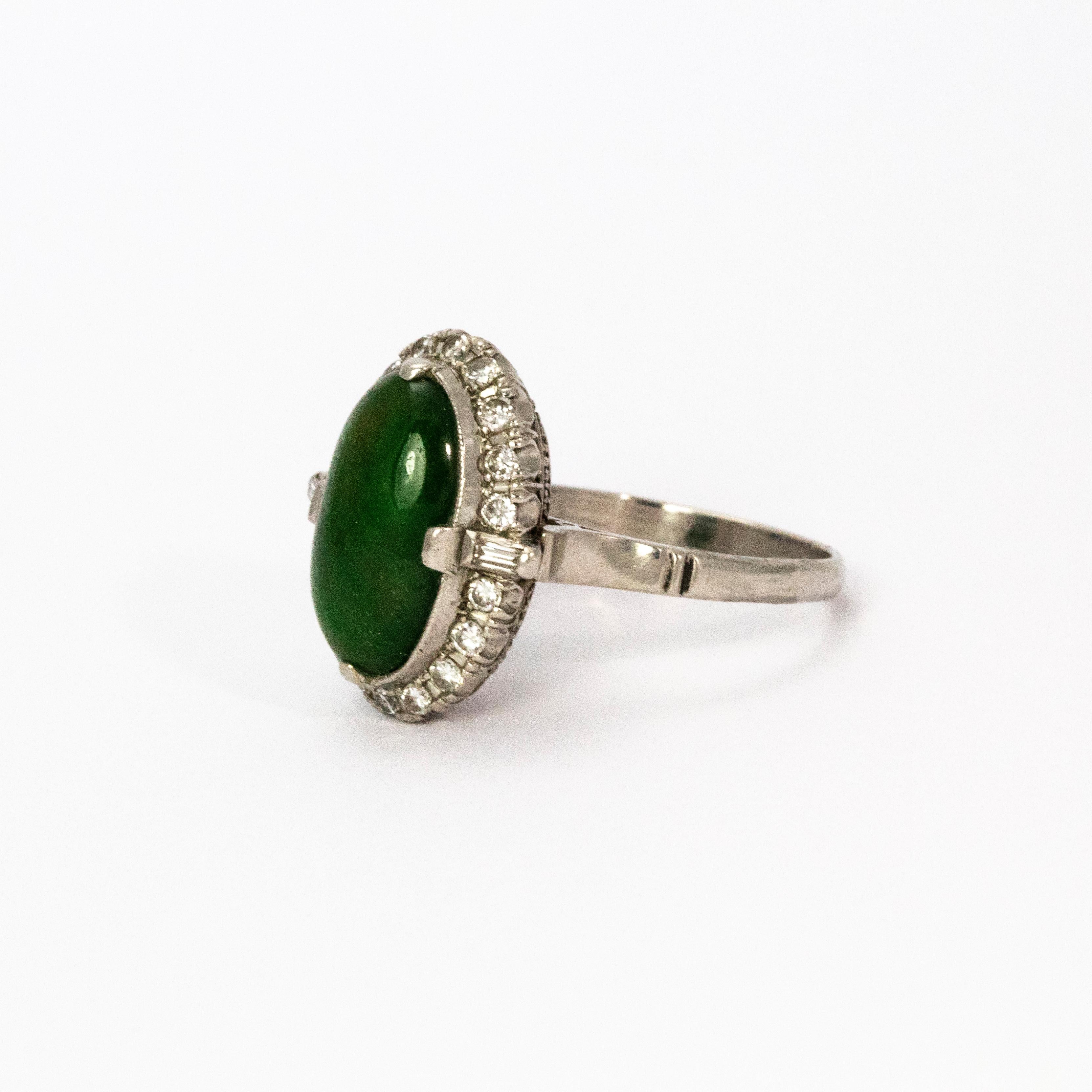 A stunning 1940s cluster ring. Centrally set with a wonderful large jade cabochon measuring approximately 4 carat, surrounded by an elegant halo of round brilliant cut diamonds. Each shoulder is set with an emerald cut diamond. Modelled in 18 karat