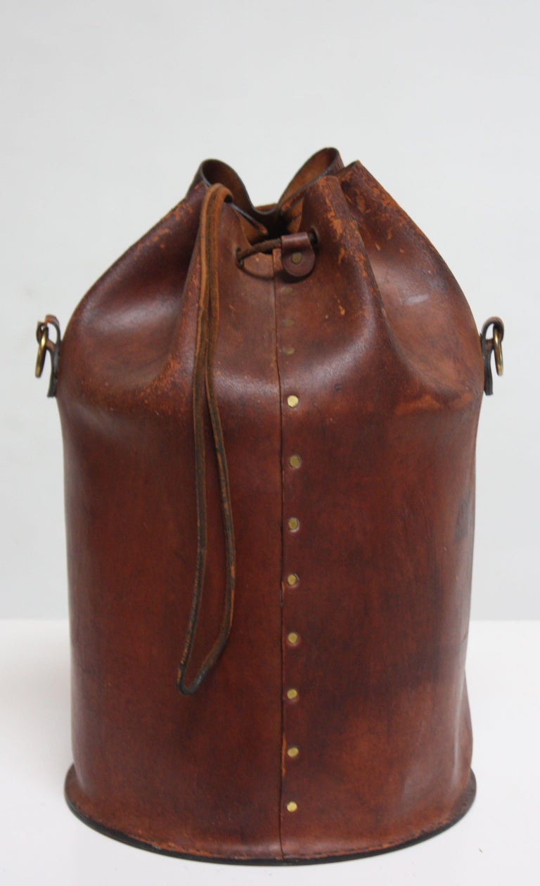 Early and rare Collins of Texas 'feed bag' composed of saddle leather trimmed in brass casting. The leather bag houses an enamel 'feed bucket,' conceived as a stylish, yet practical vessel for horse feed. Alternatively, this bucket-bag combination