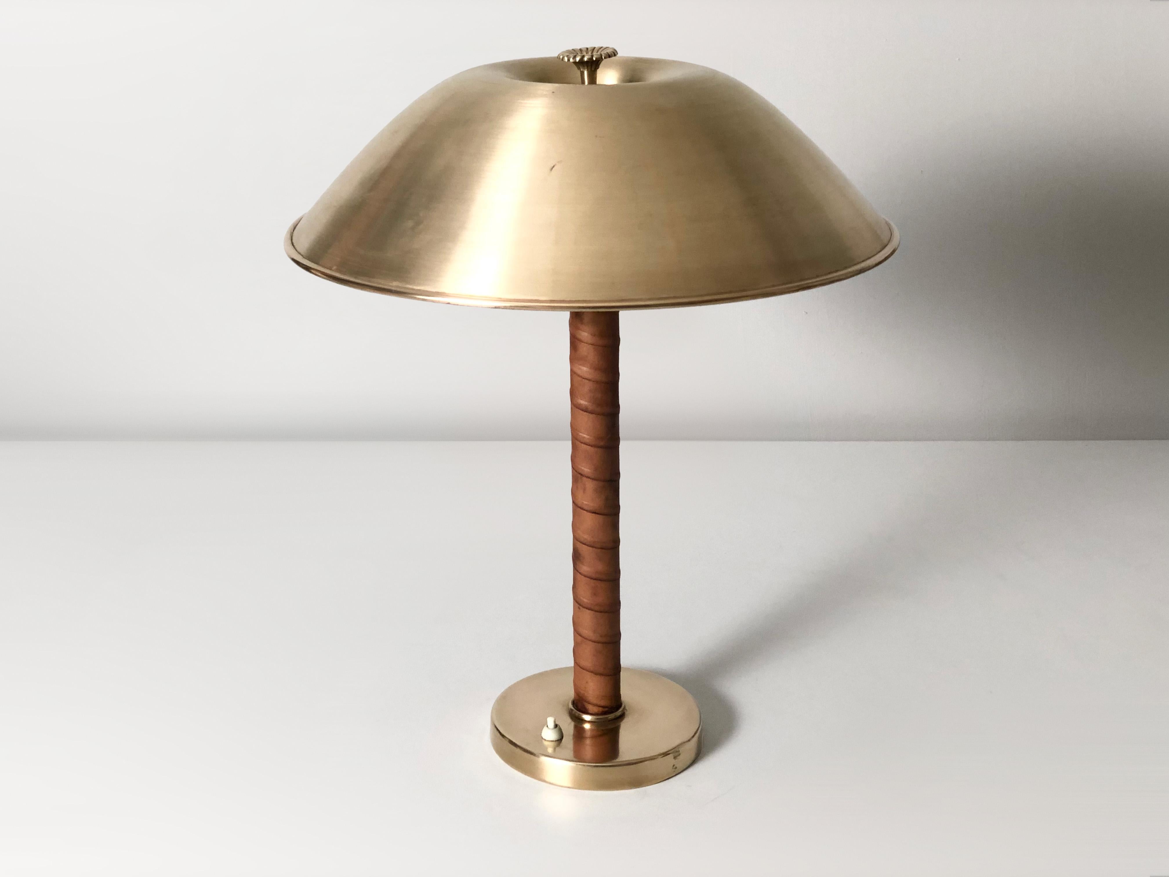 1940’s Leather Wound Brass Table Lamp By Harald Notini For NK (Nordiska Kompaniet). Cast iron base with spun brass cover, leather wound stem and spun brass lamp shade with cast brass flower shaped ornament. Holds two E27 or E26 standard Edison style