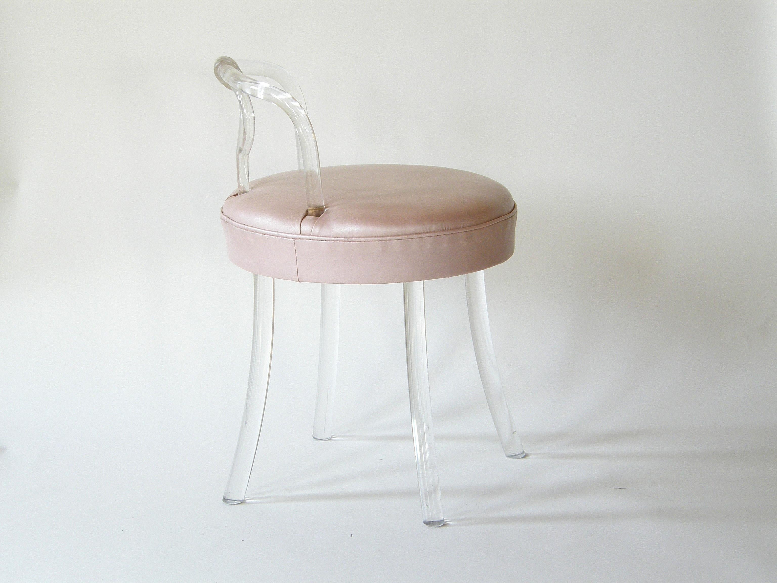 This petite vanity stool evokes the era of 1940s Hollywood glamour. The legs and backrest are made of bent Lucite, and the upholstery is a pale, dusty pink vinyl with a slightly pearlescent finish. The stool has a swiveling base for comfort and