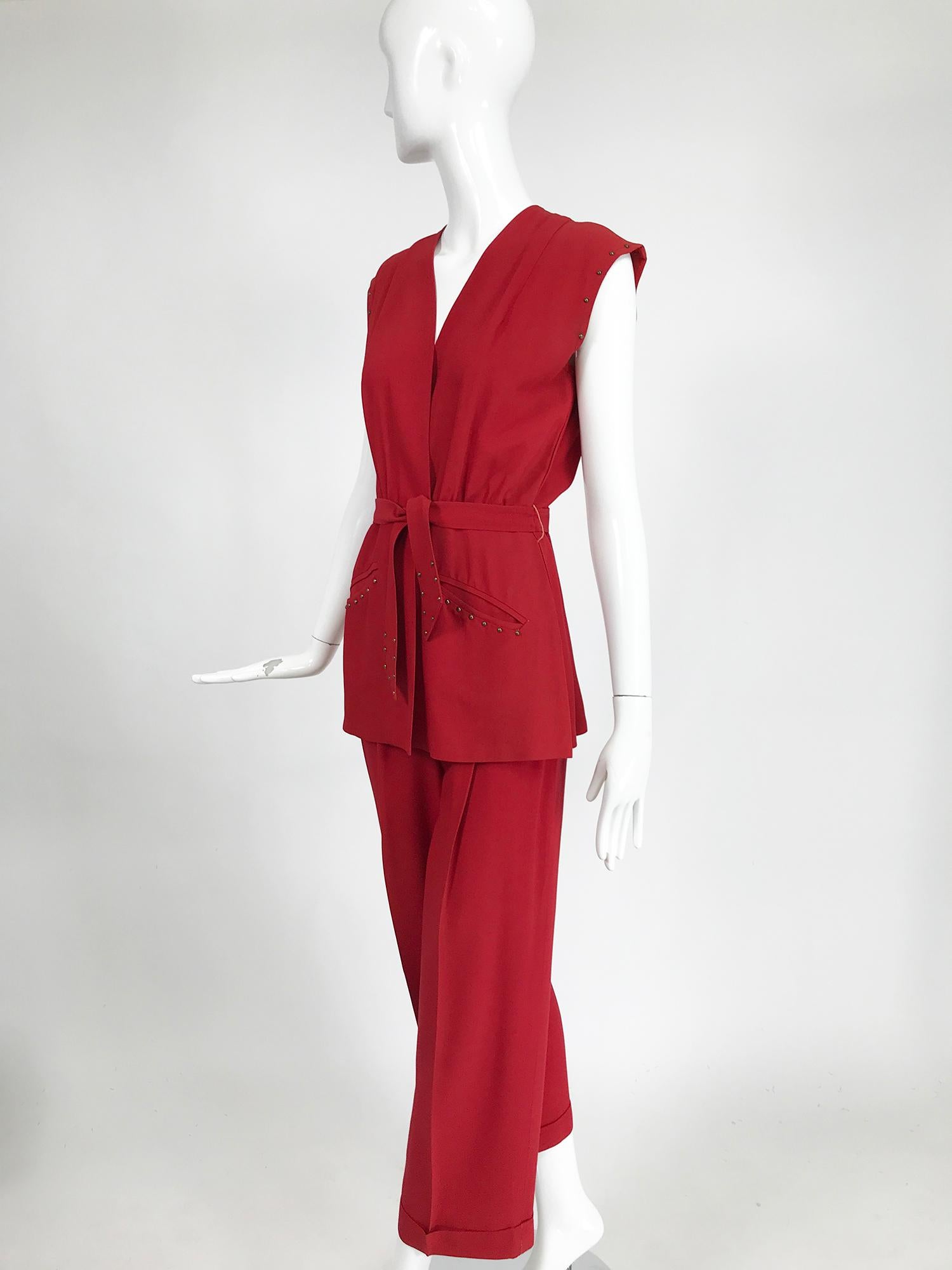 1940s Made in California, by International Sportswear, wine red rayon gabardine pant set with brass stud detail. Sleeveless wrap top features a belted waist with hidden hook and eyes, angled besom hip pockets and a peplum hem with a 7