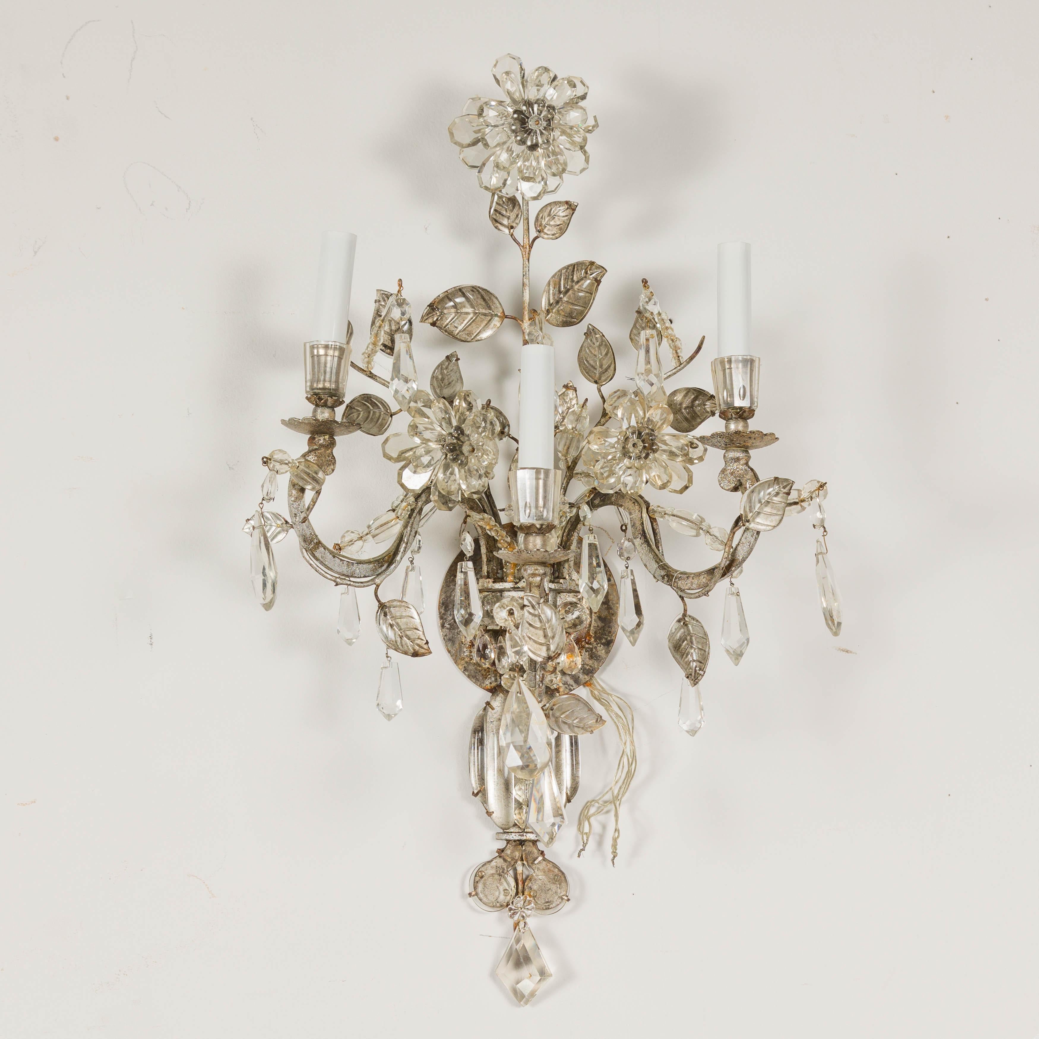 A pair of French Maison Baguès crystal sconces from circa 1940 with three arms each and floral motifs. Embodying the enduring elegance of French Maison Baguès design, this exquisite pair of crystal sconces from circa 1940 stands as a testament to