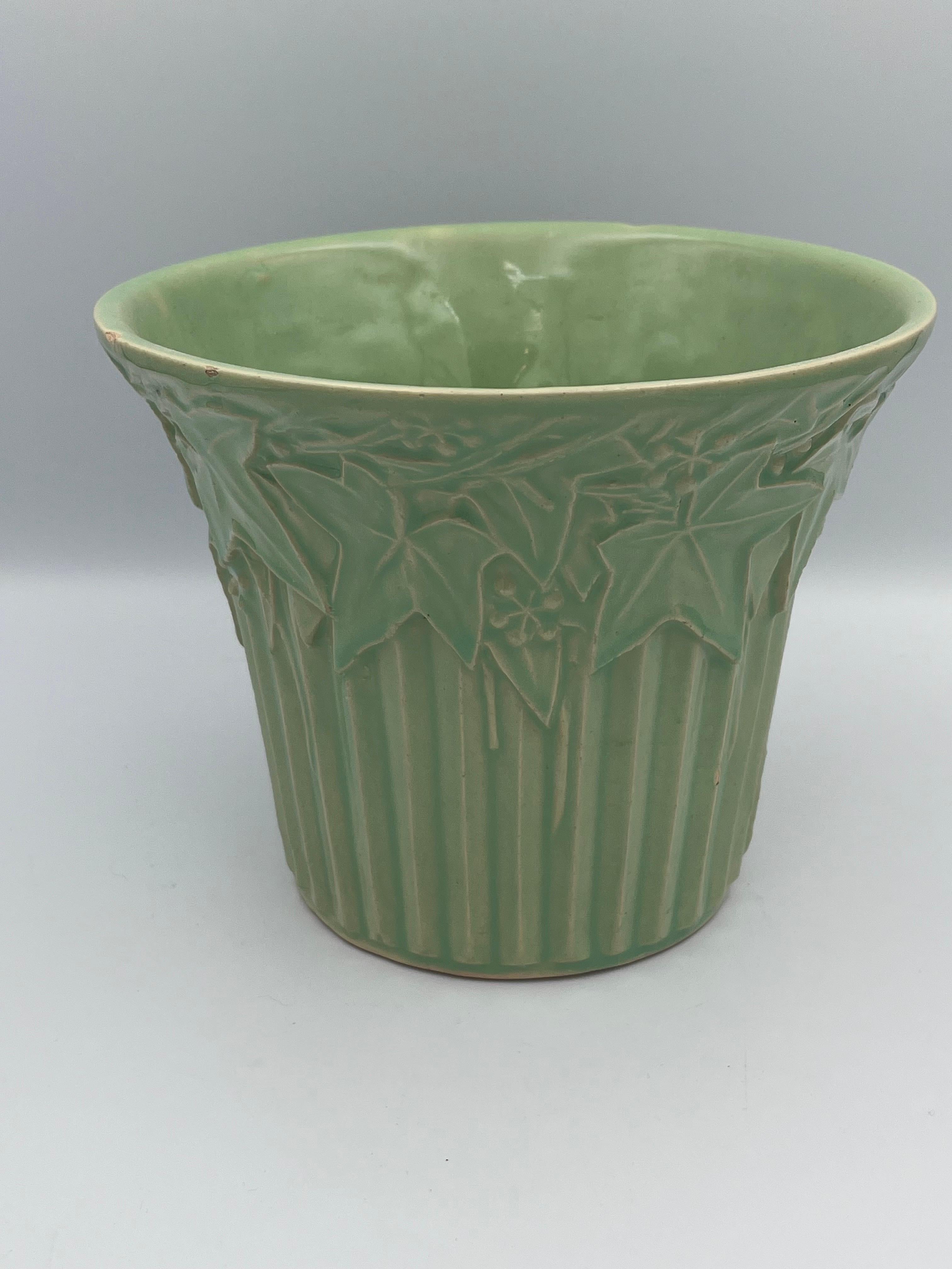 This 1940s McCoy Ivy and Berries planter in mint green embodies the timeless charm of American mid-century pottery. Featuring raised ivy and berry motifs in a fresh, glossy mint glaze, this piece showcases the functional elegance that made McCoy a