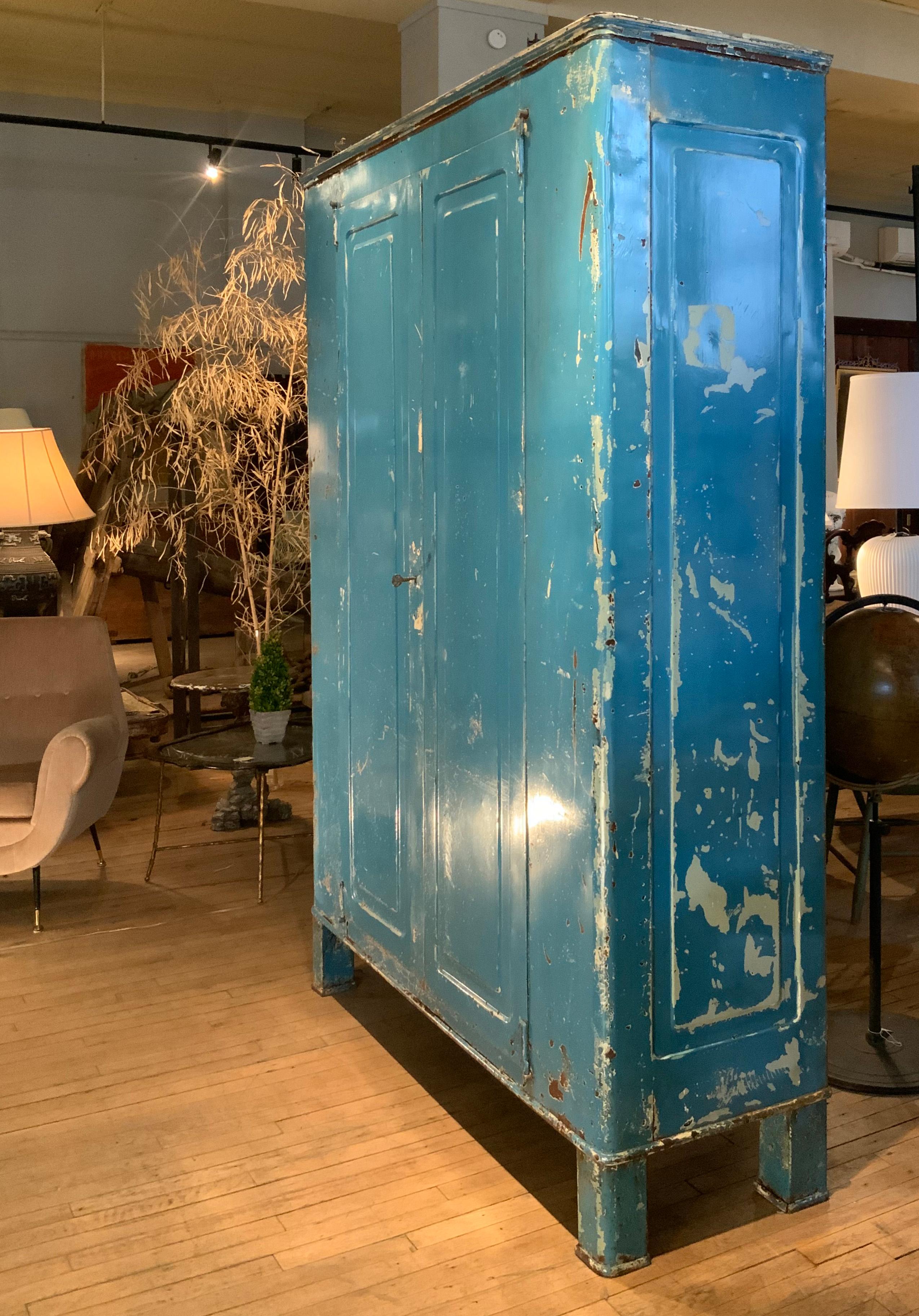 An amazing 1940's Italian steel cabinet, in its original Mediterranean Blue painted finish, with a pair of hinged doors, and a white painted interior with full width and deep shelves. the case is raised on steel legs with curved corners to match the