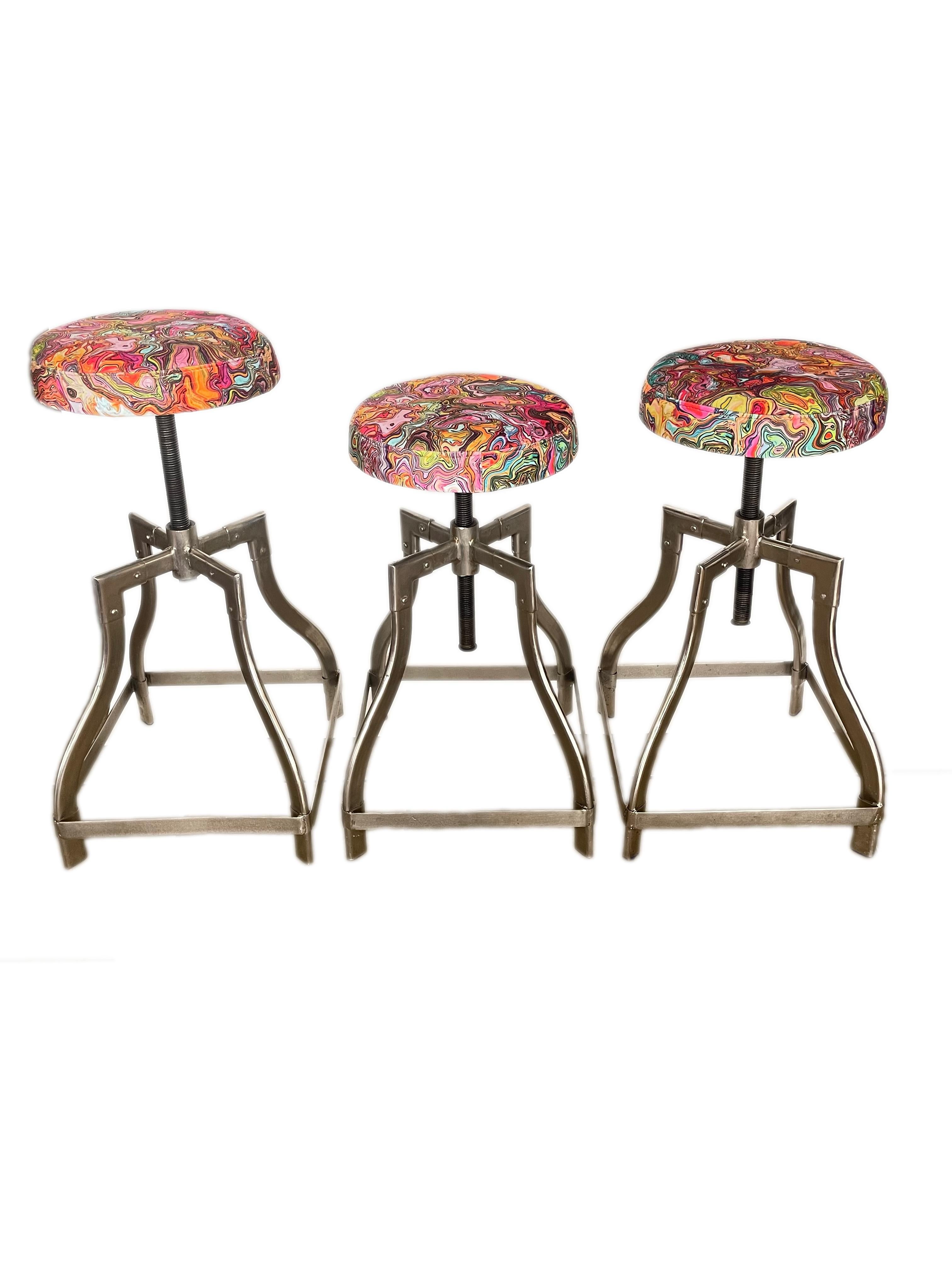 A set of three American mid-20th century steel and upholstered Industrial Swivel Stools upholstered in a bright and vibrant psychedelic upholstery with round seat and adjustable steel swivel base. The modernist, utilitarian design allows the chairs