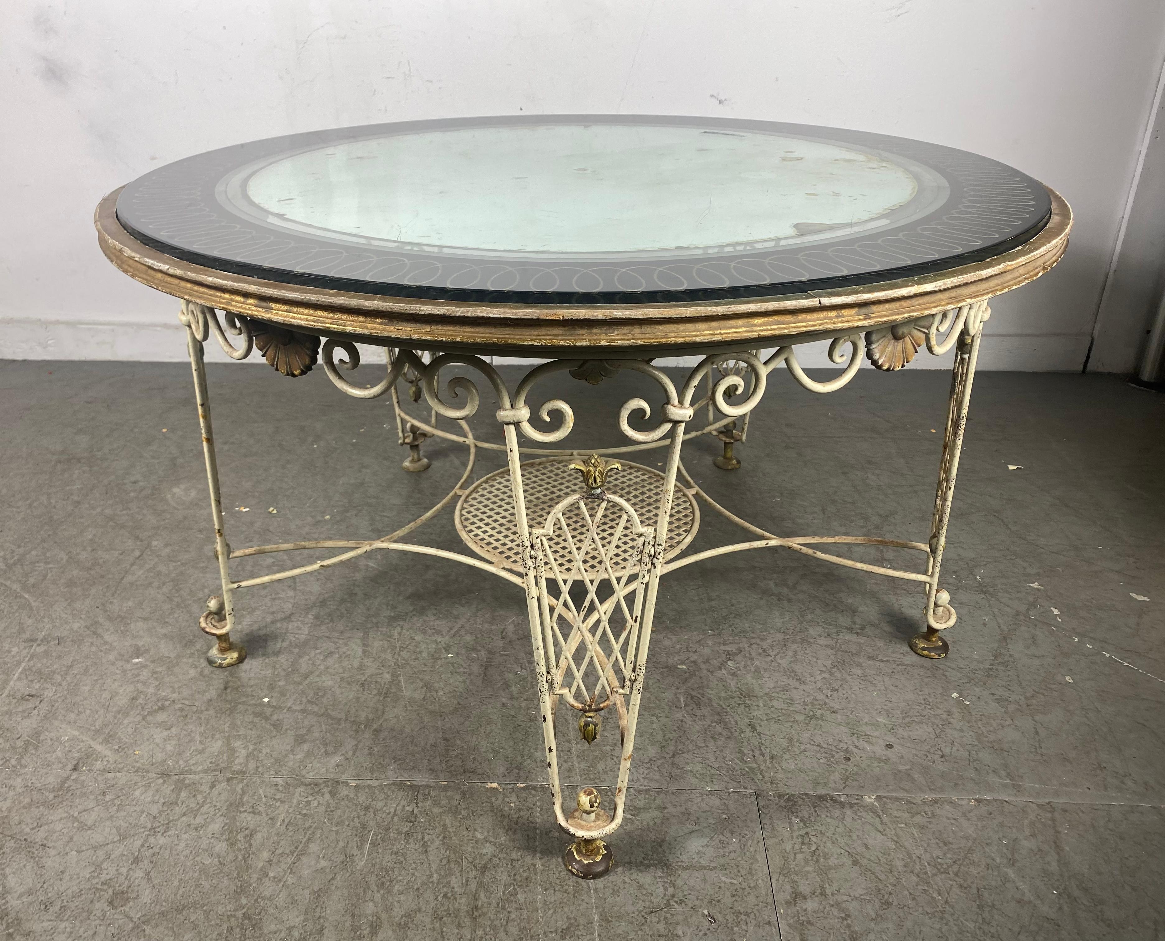Delightful and chic round coffee table with a scrolled wrought iron base with highly decorative detail and twisted gilt iron wood top surround. Gilding to base. Verre Eglomise´ mirrored table top. Blemishes and fogging to mirror top.