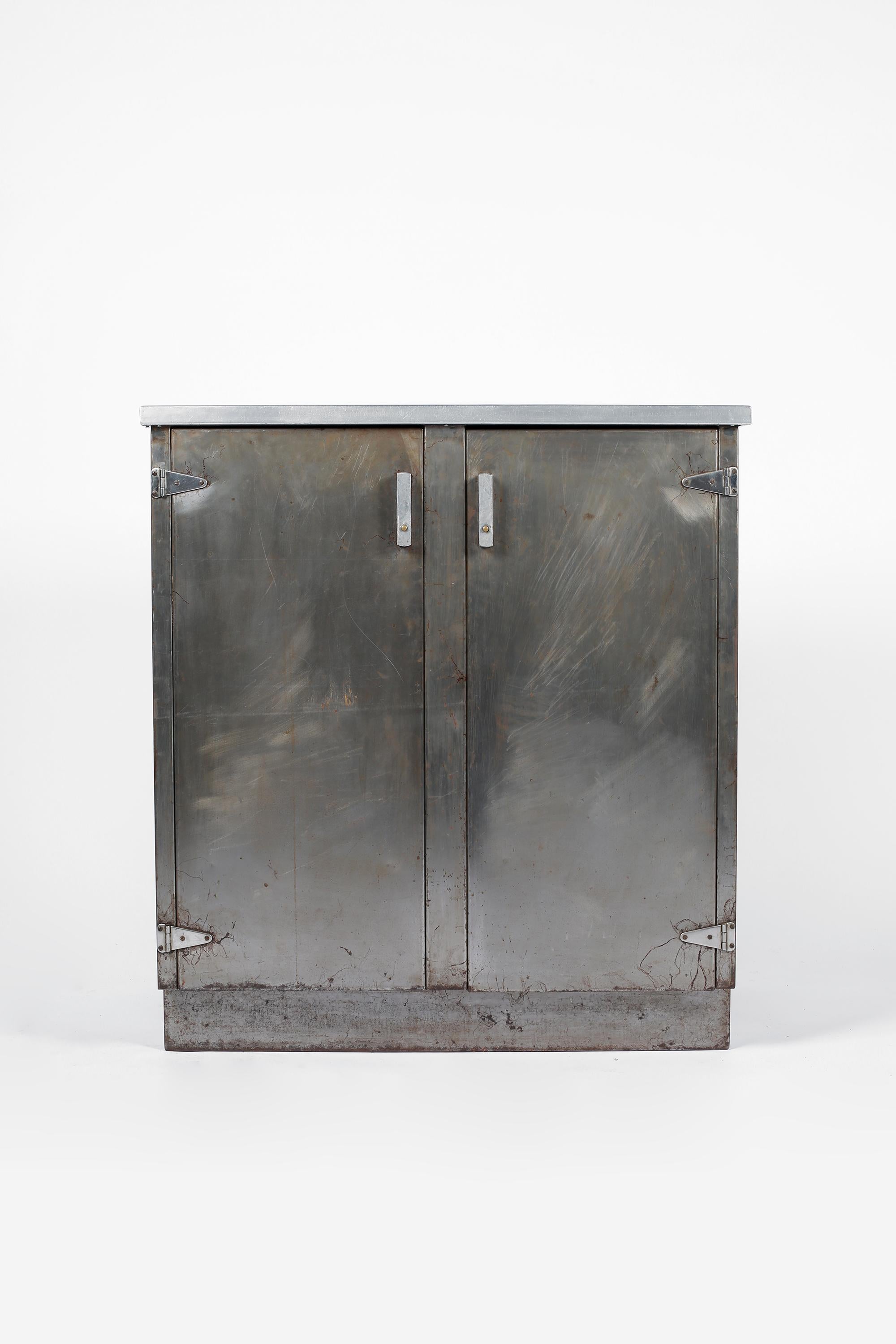 A modernist two door stripped steel cupboard with inset black linoleum top and plinth base. The shaped handles on the cupboard doors open to reveal five shelved compartments and two drawers within. English, c. 1940s.