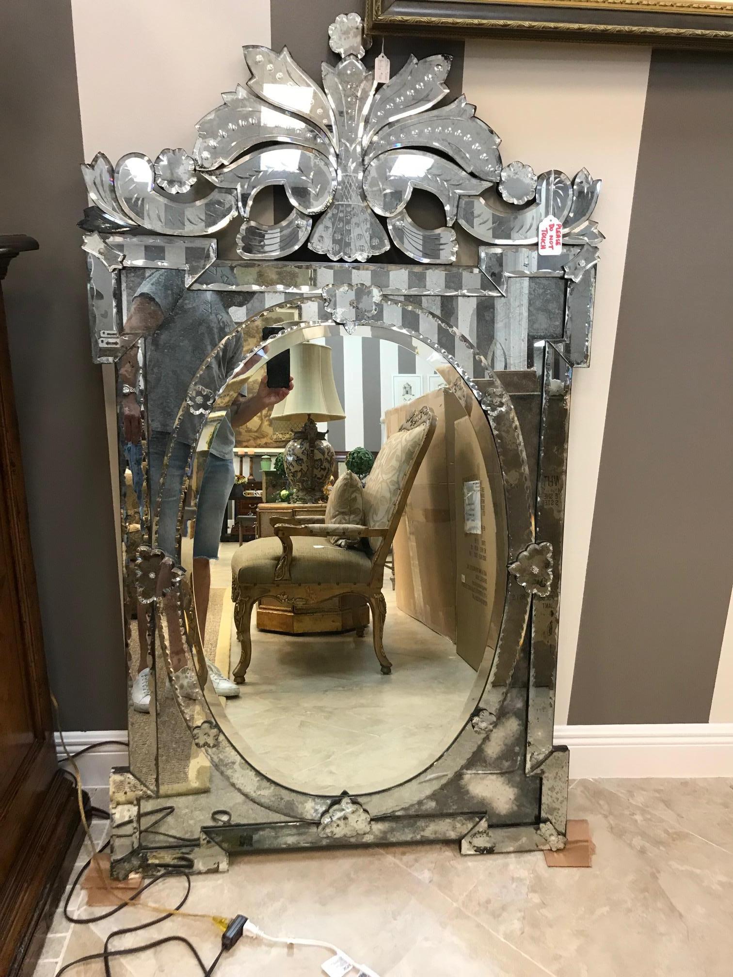 Exquisite large-scale Venetian mirror with beautiful hand etched designs throughout. The mirror features a stunning oval centre within a shield shaped frame. Pediment top features ornate scrolled designs. Has antique glass borders in hues of smoked