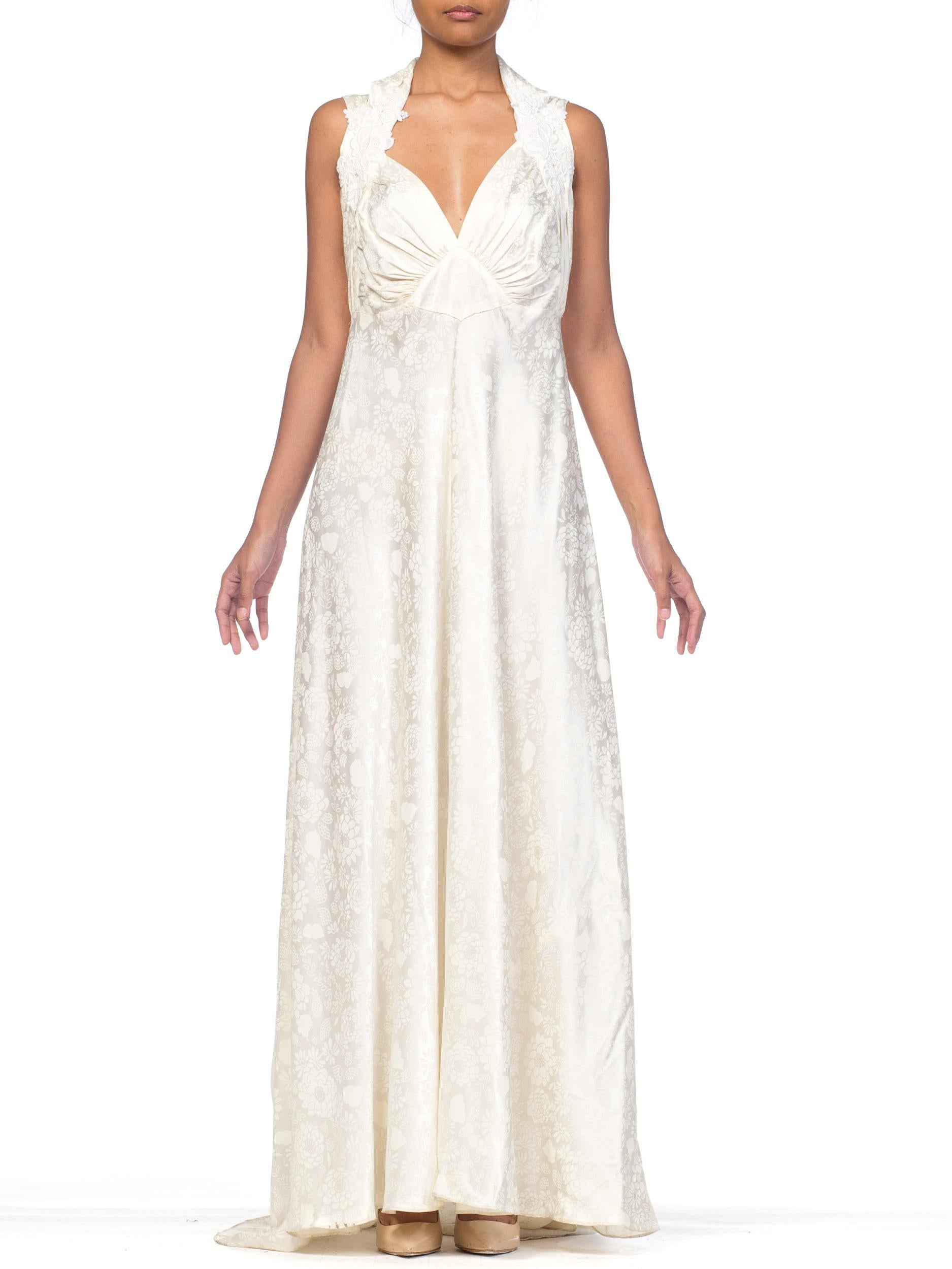 Aufgenommen an einem Modell in Größe 4 fällt dieses Kleid deutlich größer aus. Selten findet man ein Vintage-Brautkleid in dieser Größe. Es stammt aus den 1940er Jahren und ist aus weiß auf weißem, mit Blumen bedrucktem Satin. Von uns in Handarbeit