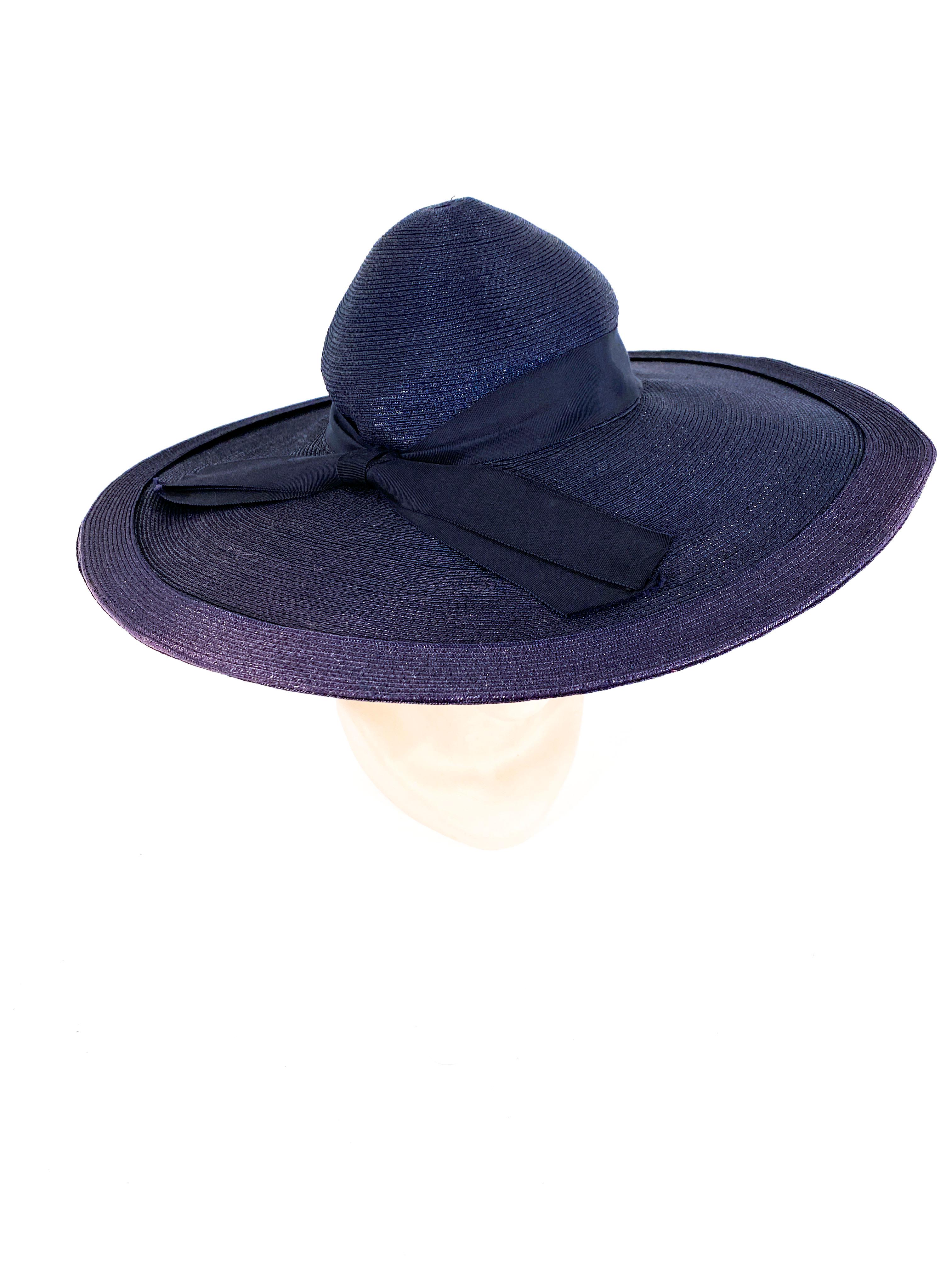 1940s Navy wide brimmed-hat made of a woven and coated straw. The wide brim is trimed with a secondary ring of straw, the high crown is adorned with a grosgrain ribbon, woven patterned button, and an enlarged bow. The crown is small as this hat is