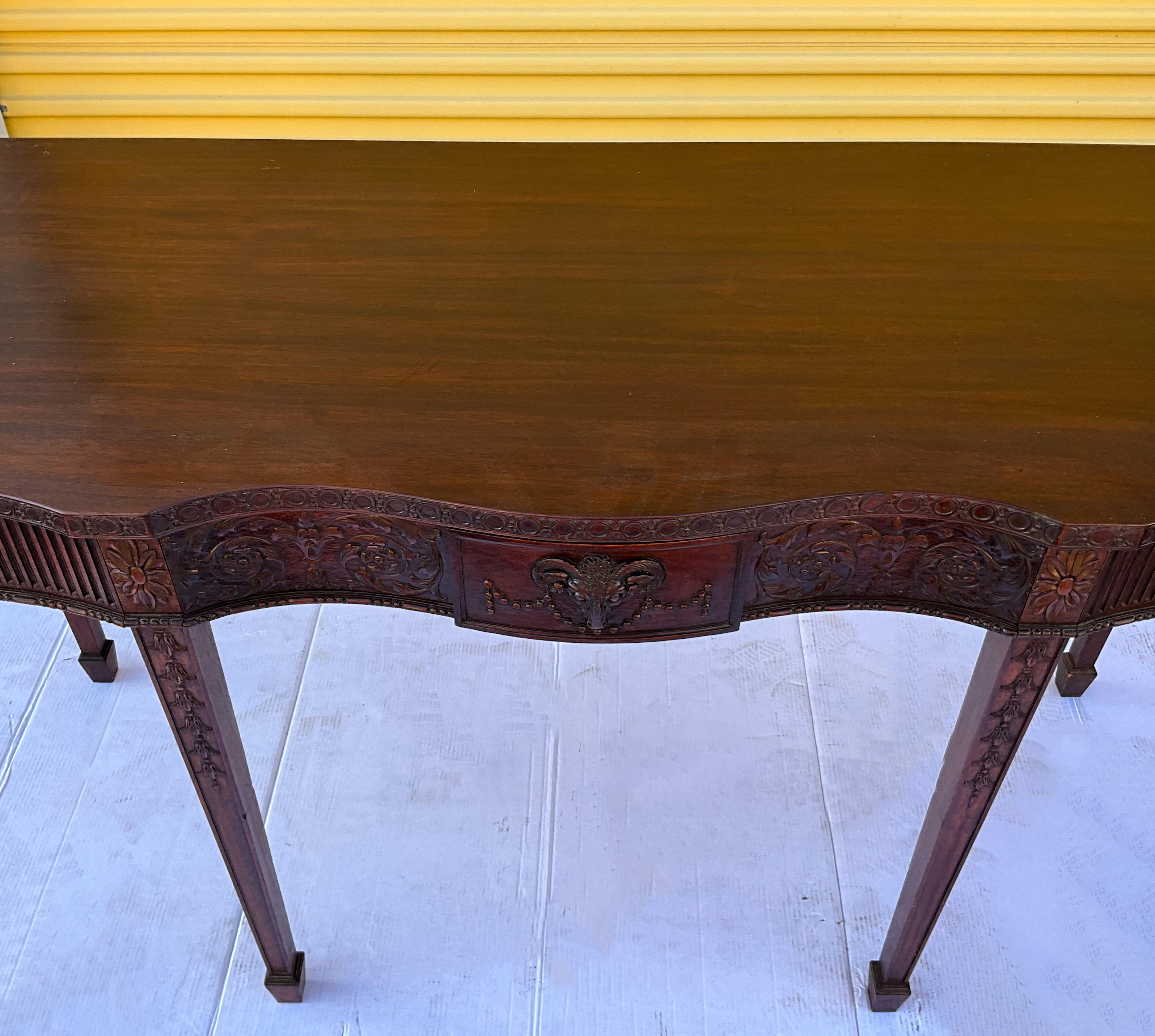 This is a statement piece! This is a 1940s carved mahogany hunt board with a sculpted top and a single drawer with dovetail construction. It has a carved ram’s head as well as other Greco - Roman elements. The tapered legs have spade feet.