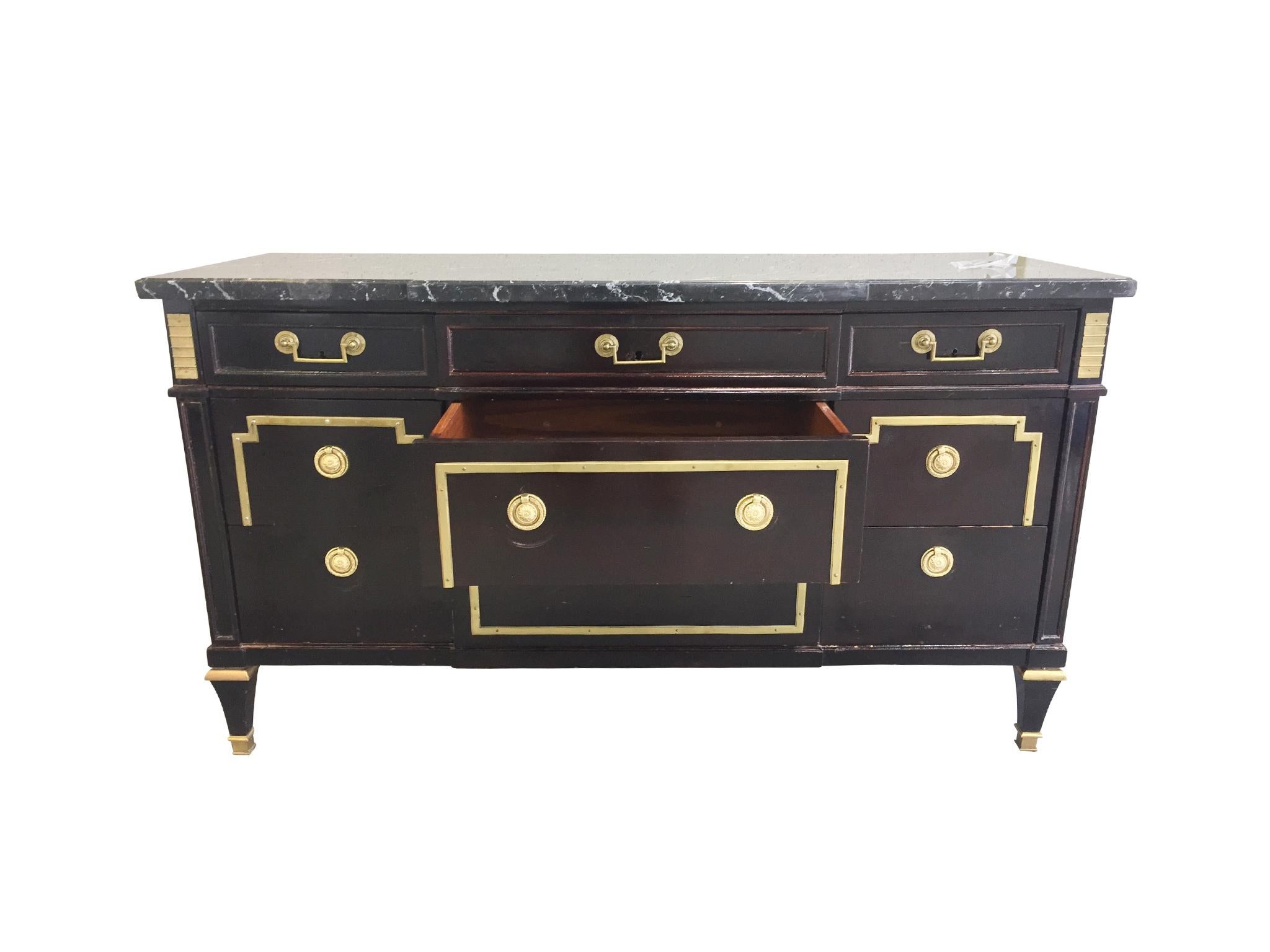 An elegant 1940s chest of drawers consisting of lacquered wood, gilt detailing, and a marble top. It is designed in a neoclassical style. The wood has a warm dark-brown color, while the trims and pulls are gilt metal that beautifully complements the