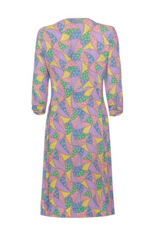This pretty 1940's rayon crepe dress features a whimsical patchwork/bunting novelty print in soft pastel shades of yellow, blue, pink, purple and green. It is comprised of asymmetric panels with the wrap over skirt gathered up at the waist and