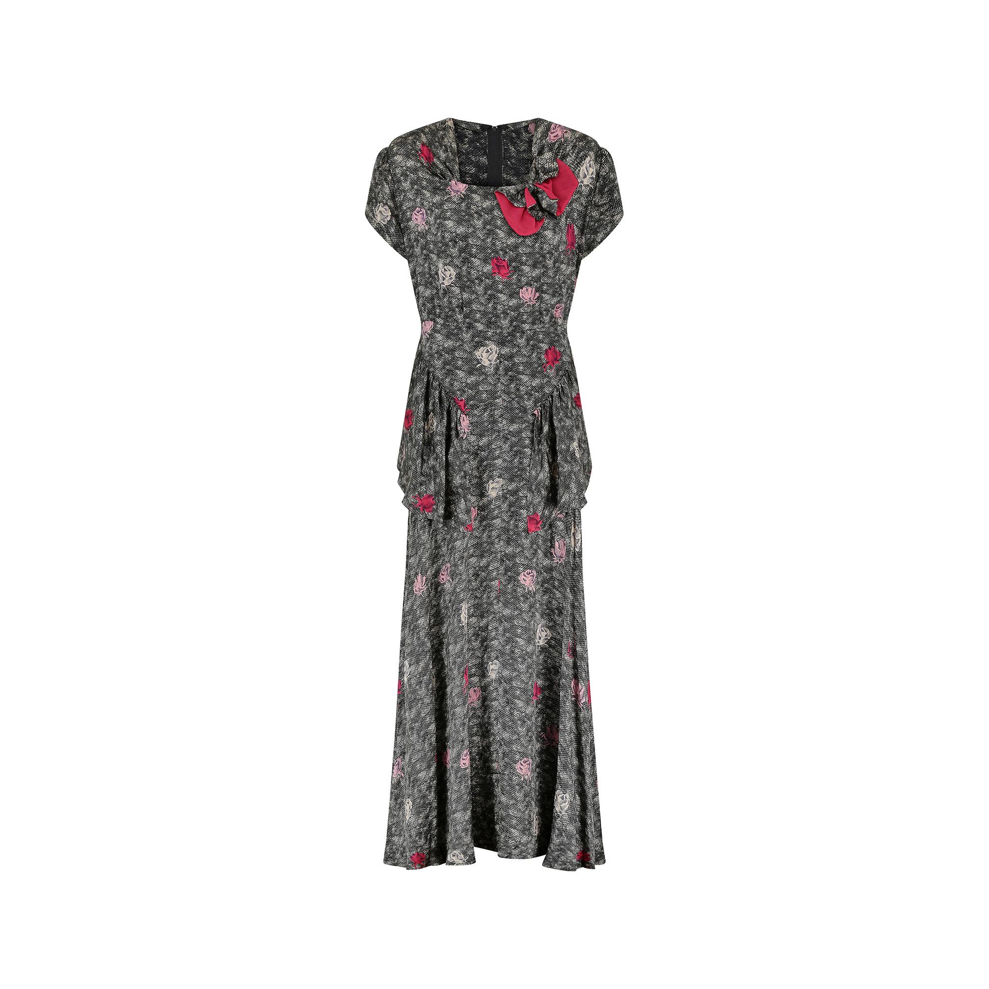 This superb and original 1940s silk peplum floor length dress is crafted from an exceptionally high-quality silk fabric with crepe accents. It has capped sleeves and a square neckline, with a 3D bow detail to the left side of the chest. This bow is