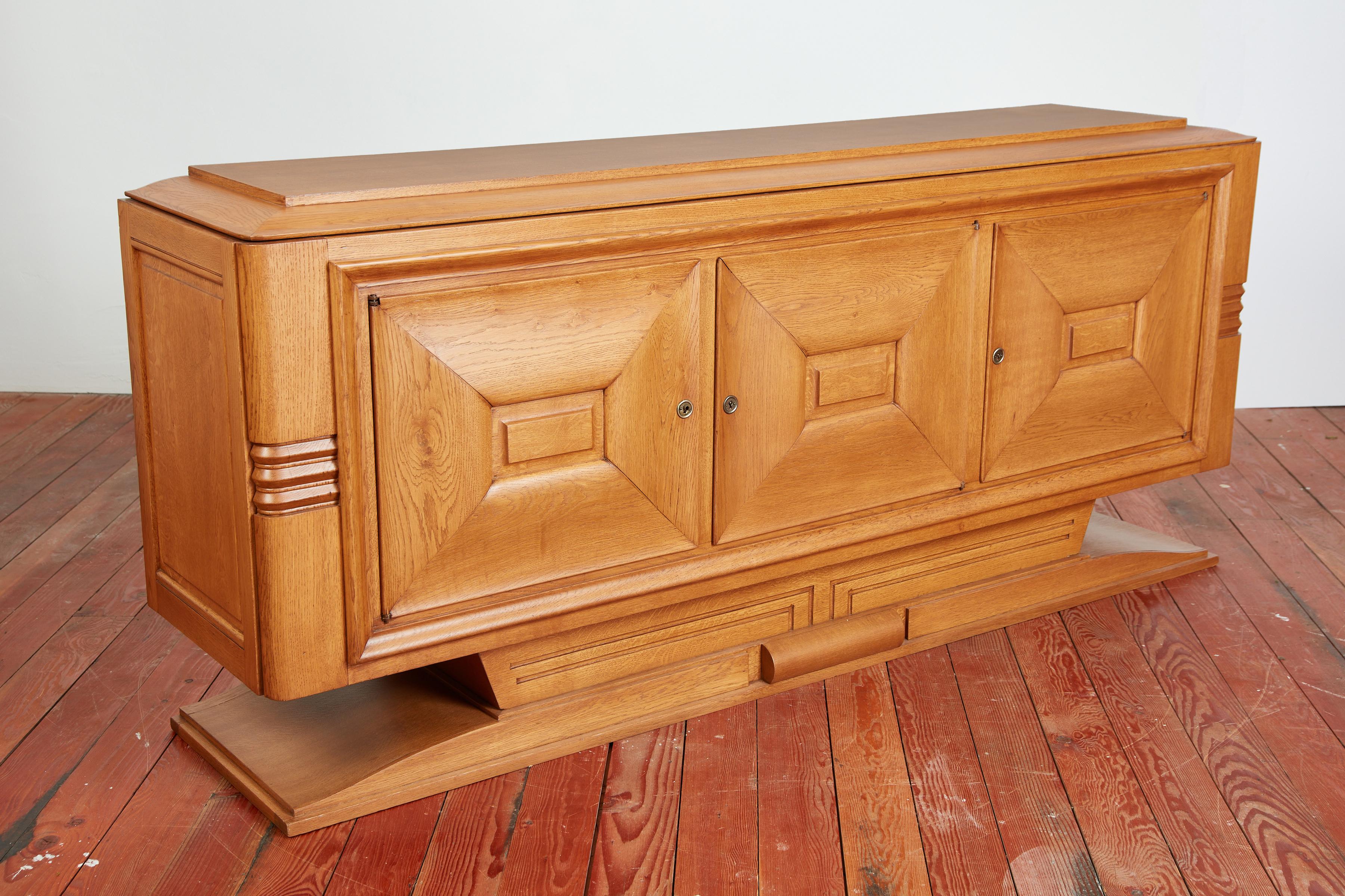 Simple oak sideboard with clean linear lines - floating on angular pedestal base. 
France, 1940's 
3 individual doors to open shelving with small drawer
Carved detail throughout and wonderful patina restored to be as good as new! 