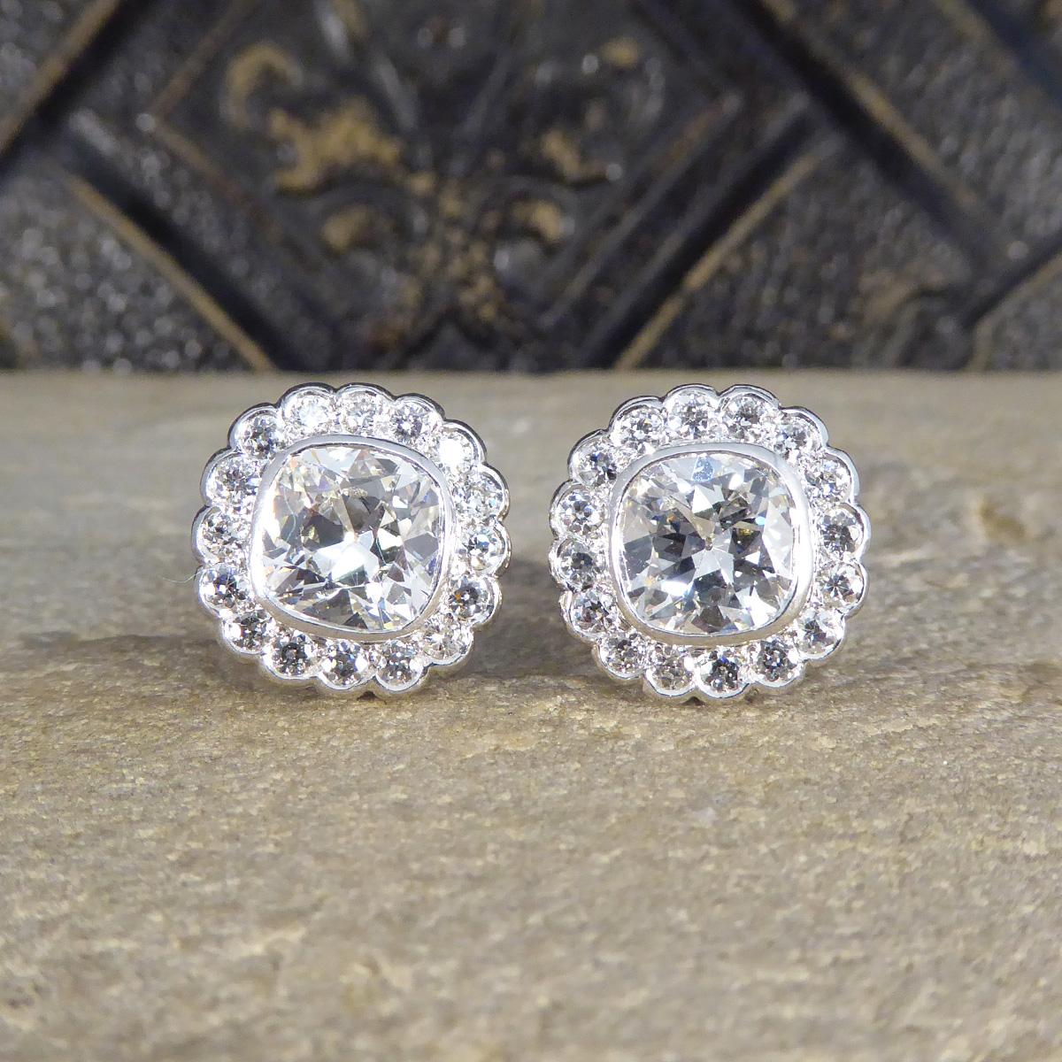 Emanate timeless elegance with these exquisite 1940's Old Cushion Cut Daisy Cluster Stud Earrings, masterfully crafted in luxurious platinum. At the heart of each stud lies a captivating approximately 2.00ct cushion cut diamond, boasting an